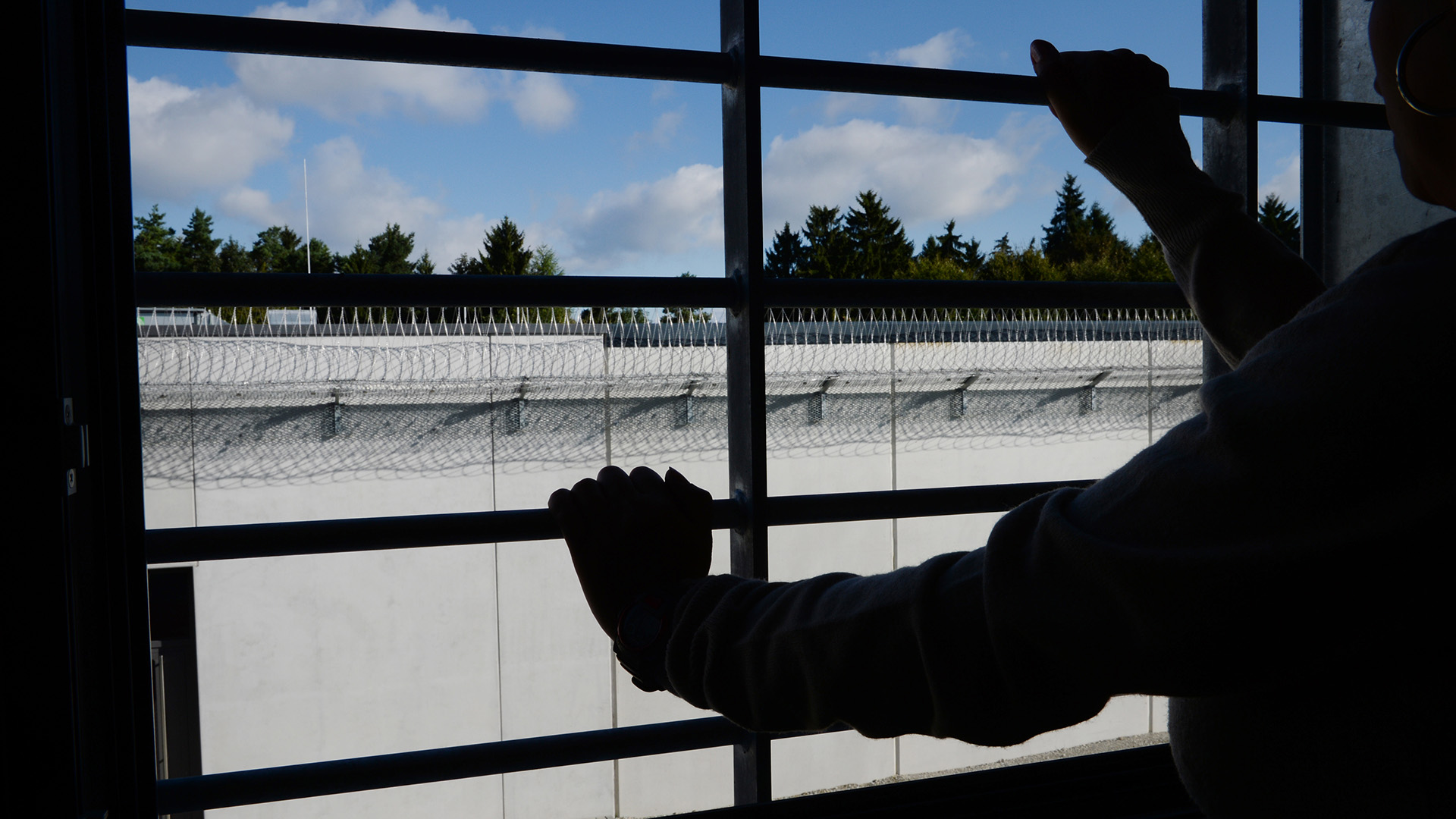Ein Gefängnisinsasse sitzt vor einem vergitterten Fenster.
