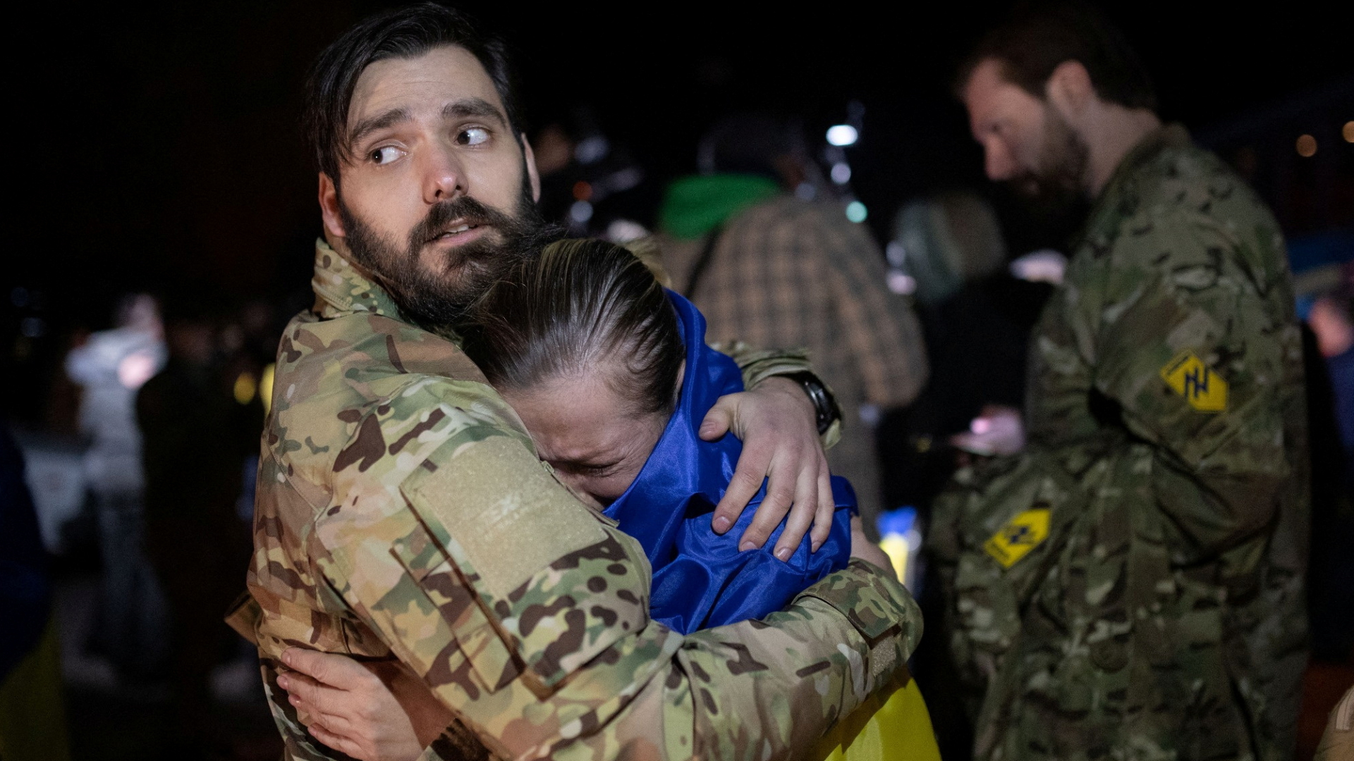 Ein Mann in Saporischschja schließt eine in die ukrainische Fahne gehüllte Kriegsgefangene in die Arme. | via REUTERS