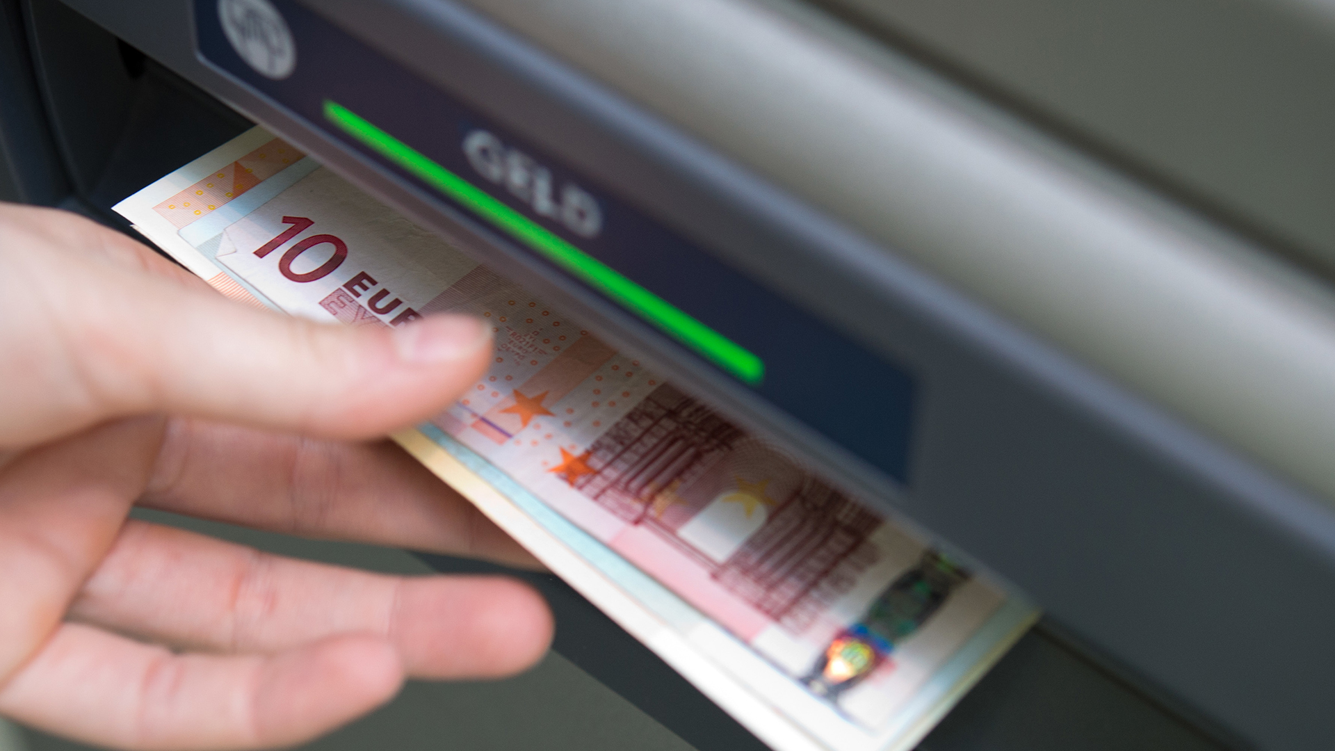 Eine Hand greift nach Geldscheinen, die aus einem Geldautomaten ausgeworfen wurden | dpa