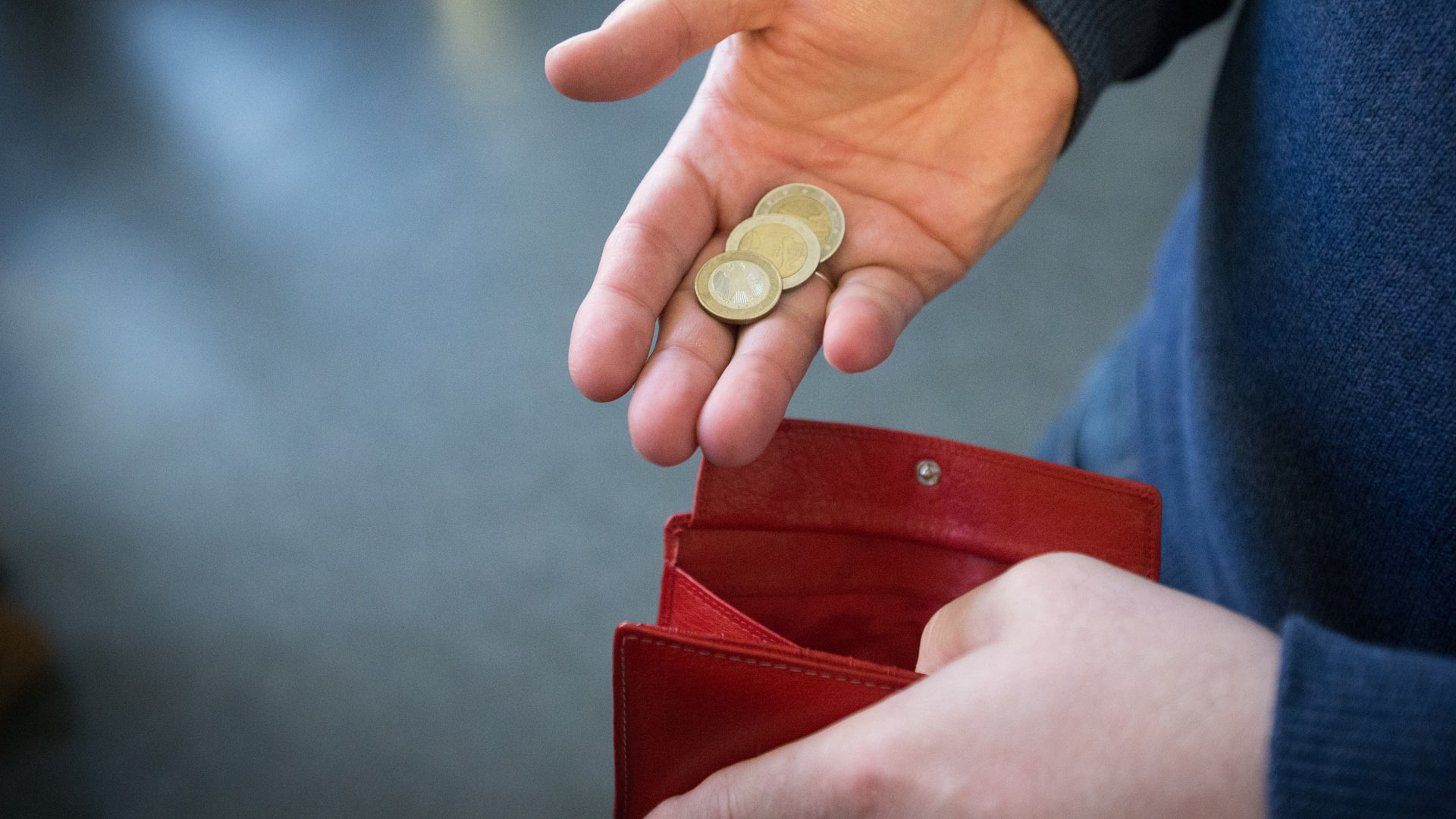 Münzen im Wert von fünf Euro über ein rotes Portemonnaie gehalten.