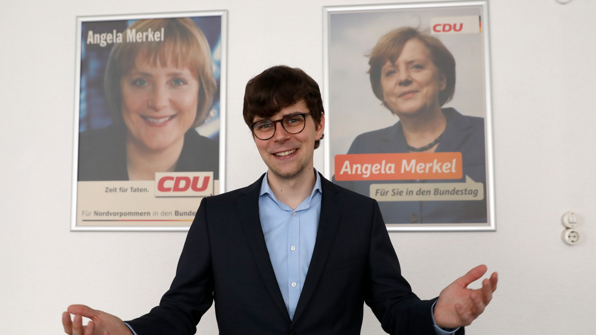 Georg Günther steht vor zwei Wahlplakaten von Angela Merkel. | dpa