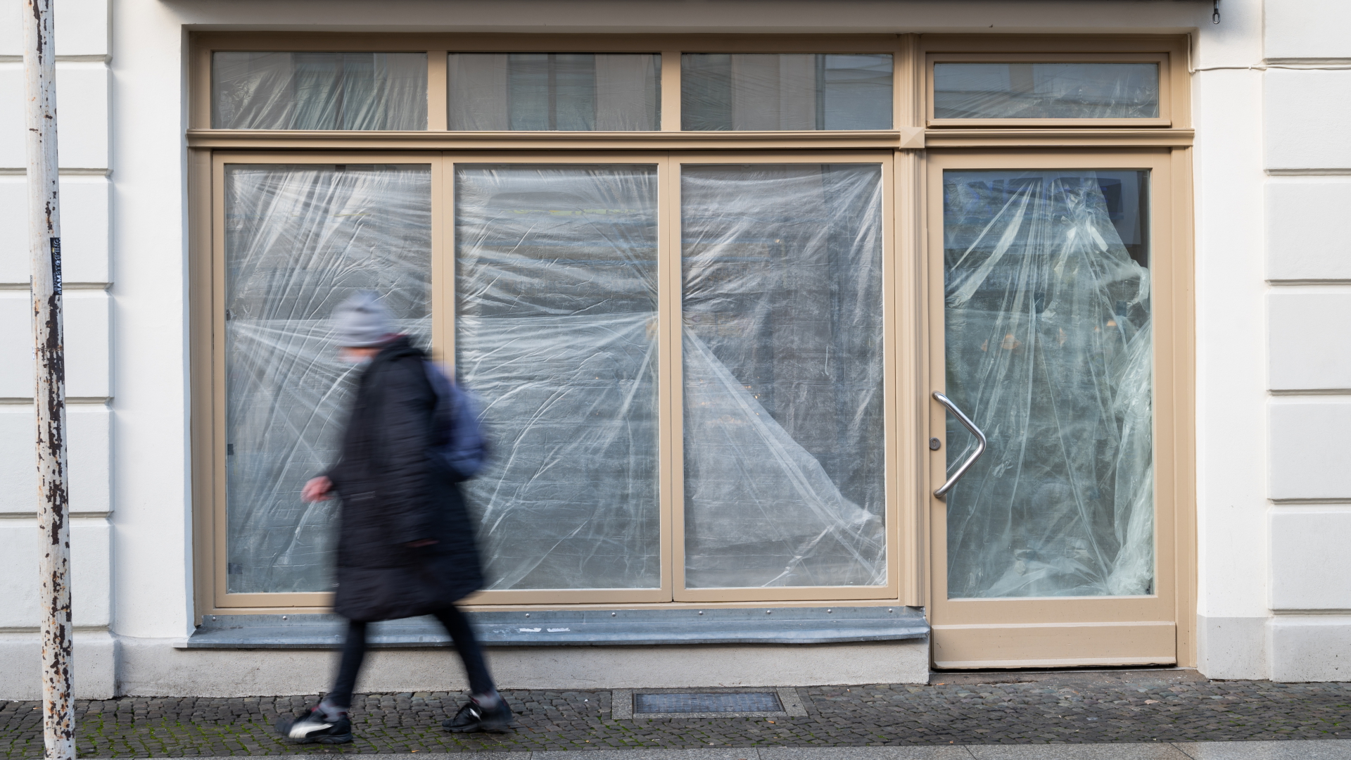 In der Potsdamer Fußgängerzone geht eine Passantin an einem Laden vorbei, der mit Plastikplane verhängt ist. | dpa
