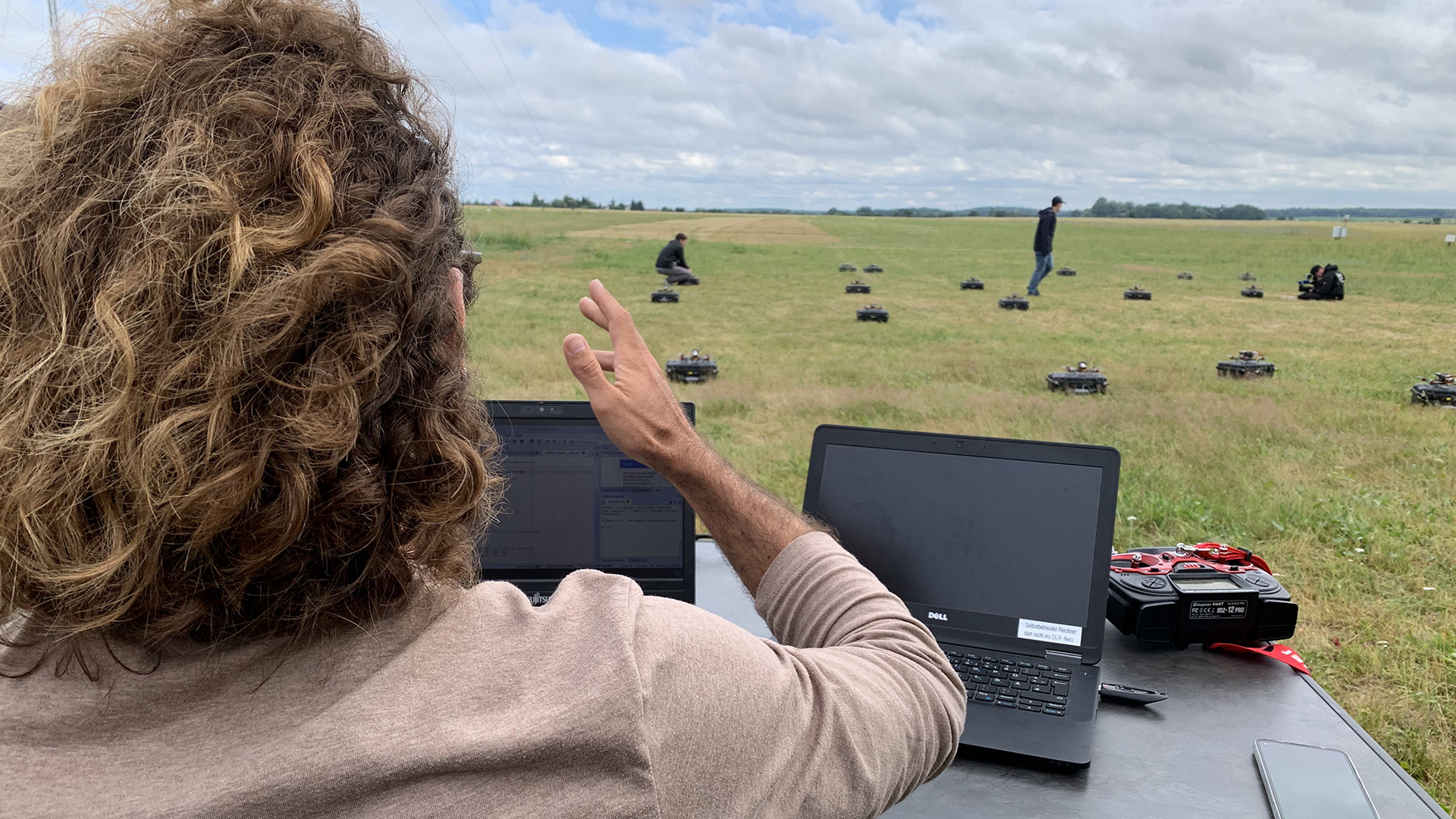 Ein Forscher am PC überwacht die Drohnen, die auf der Wiese verteilt stehen. | Alex Jakubowski/HR