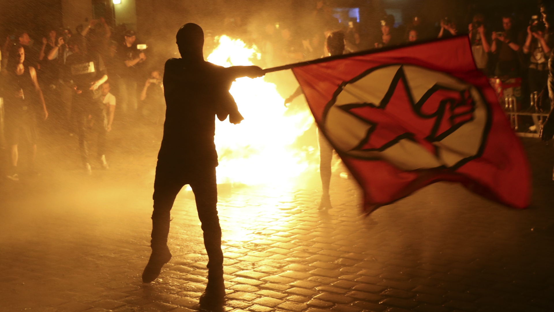 Ein Demonstrant schwingt vor brennenden Barrikaden eine Protestflagge. | REUTERS