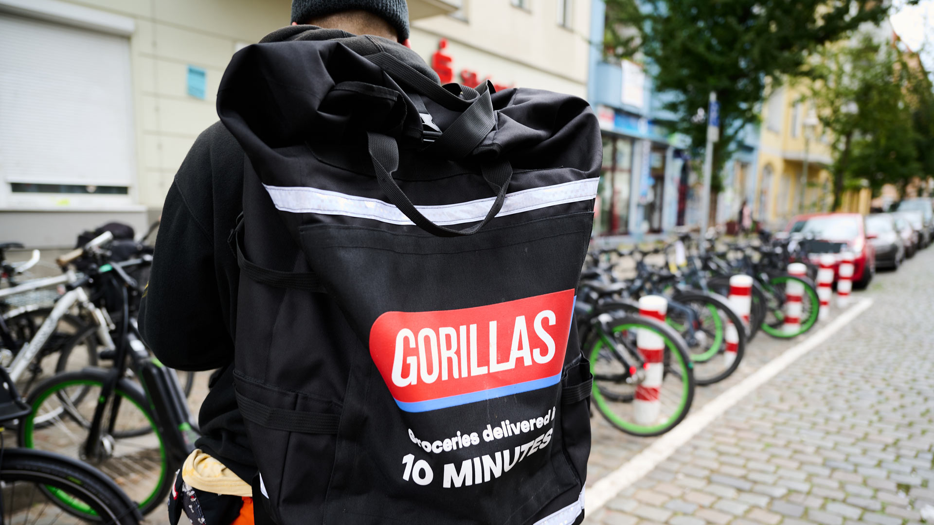 Ein Beschäftigter des Lieferdienstes Gorillas trägt einen Rucksack und steht vor den Fahrrädern | picture alliance/dpa