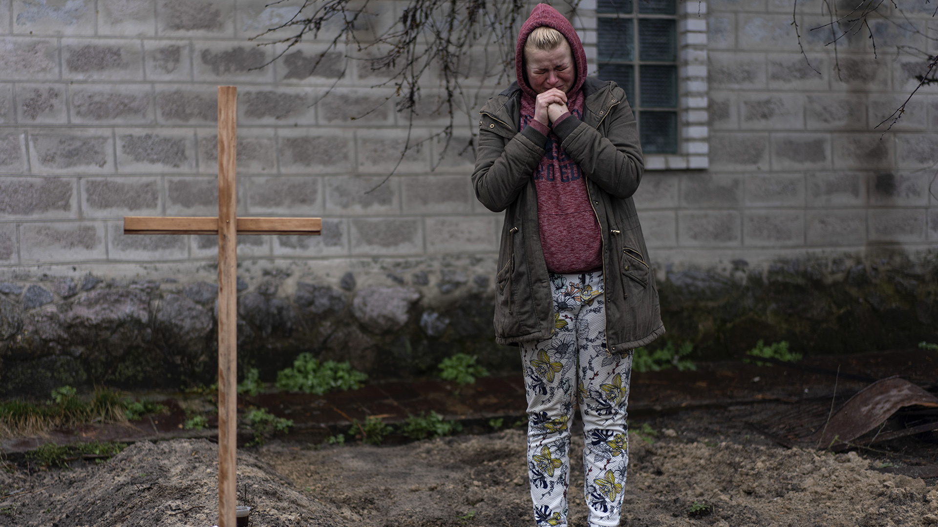 Eine Frau mit gefalteten Händen und schmerzverzerrtem Gesicht steht neben einem Holzkreuz. | dpa