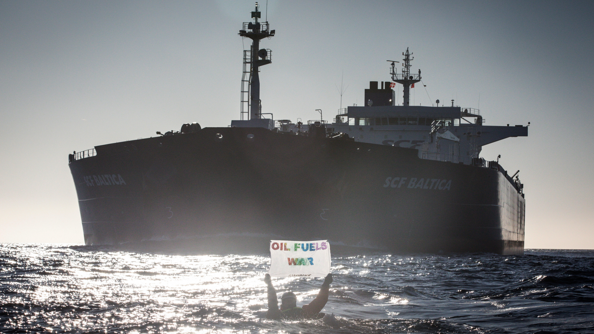Ein Greenpeace-Aktivist hält in der Ostsee ein Protestschild vor einem russischen Tanker in die Luft. | dpa
