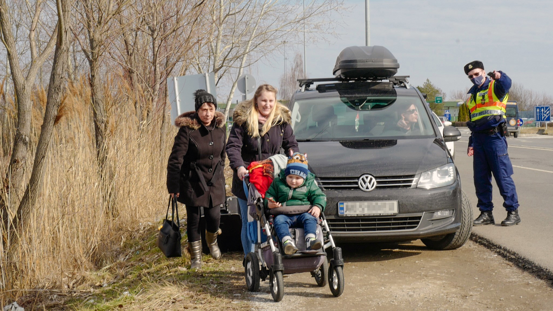 Großmutter, Mutter und Kleinkind sind auf ungarischem Gebiet angekommen, daneben steht ein Auto, dessen Fahrer von einem Grenzbeamten Auskunft erhält. | BR/Wolfgang Vichtl
