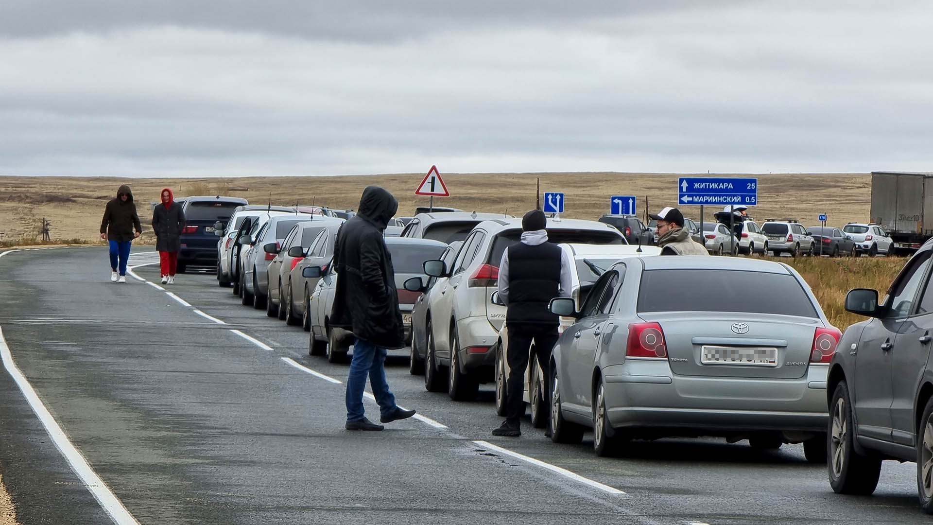 Menschen gehen neben ihren Autos in der Warteschlange für den Grenzübertritt nach Kasachstan am Grenzübergang Mariinsky.  | picture alliance/dpa/AP