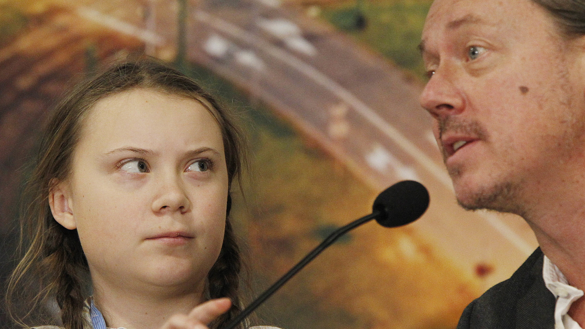 Greta Thunberg (li.) steht neben ihrem Vater an einem Rednerpult. | dpa