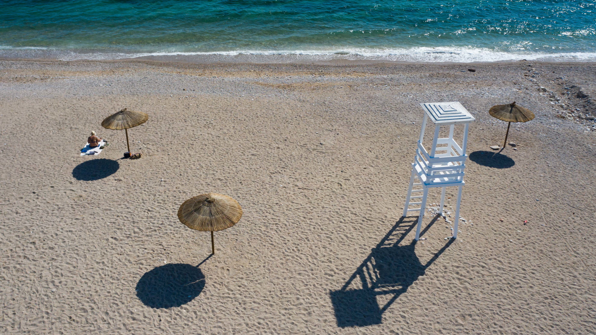 Eine Frau sitzt an einem sonst verlassenen Strand nahe Athen. | dpa