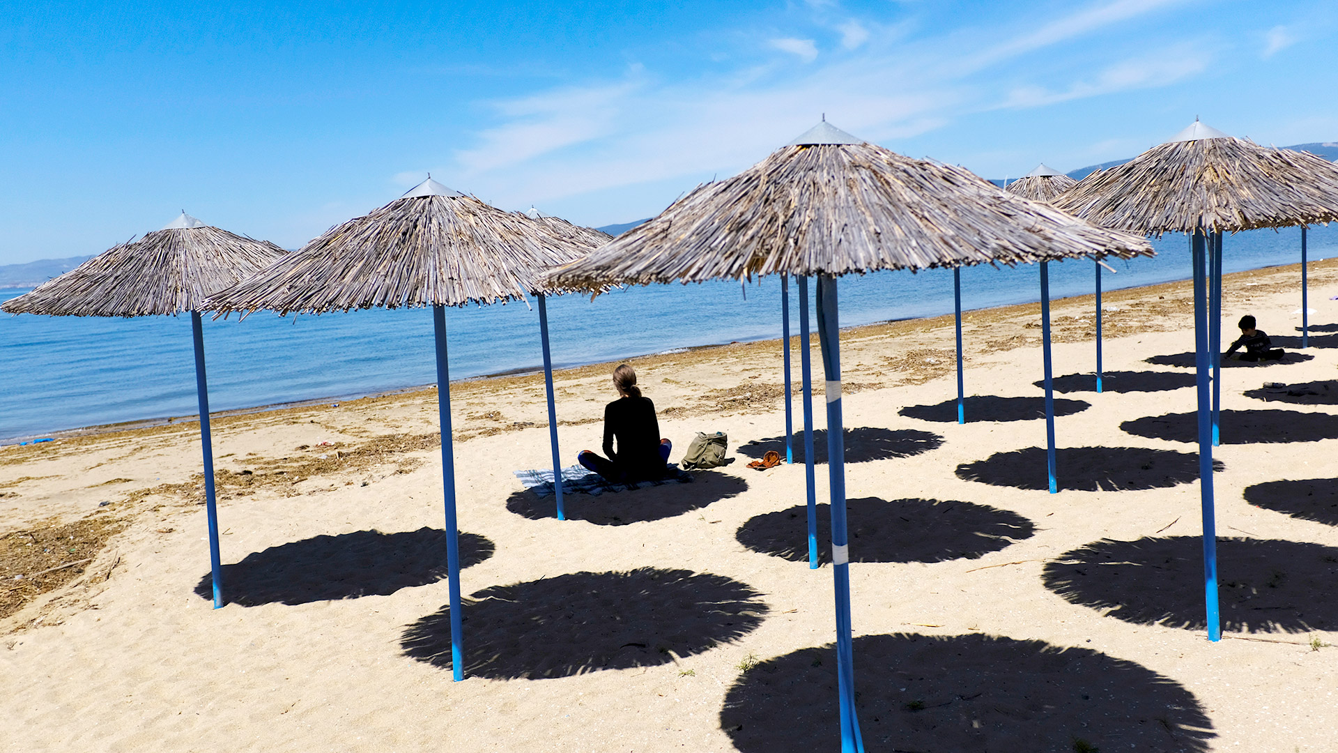 Eine Frau sitzt am leeren Strand von Peraia in Griechenland. | REUTERS