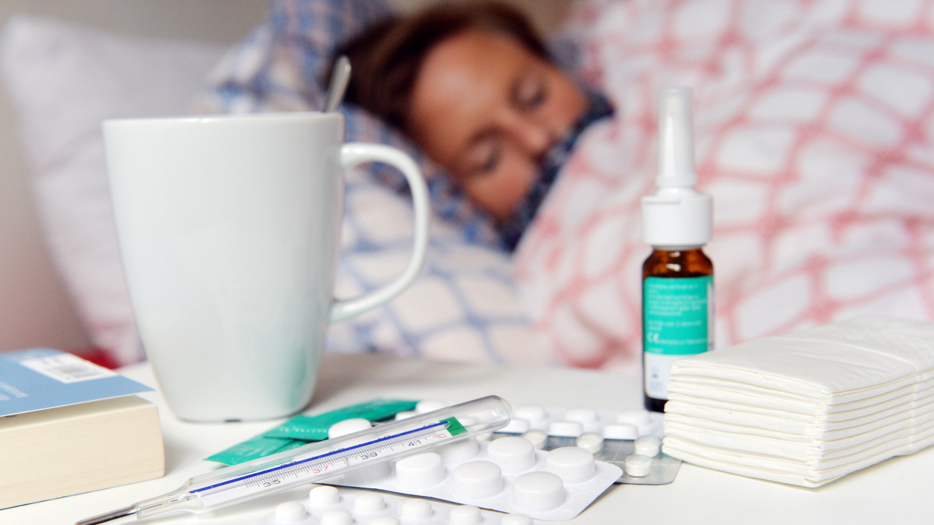 Medikamente und ein Fieberthermometer liegen auf einem Nachttisch