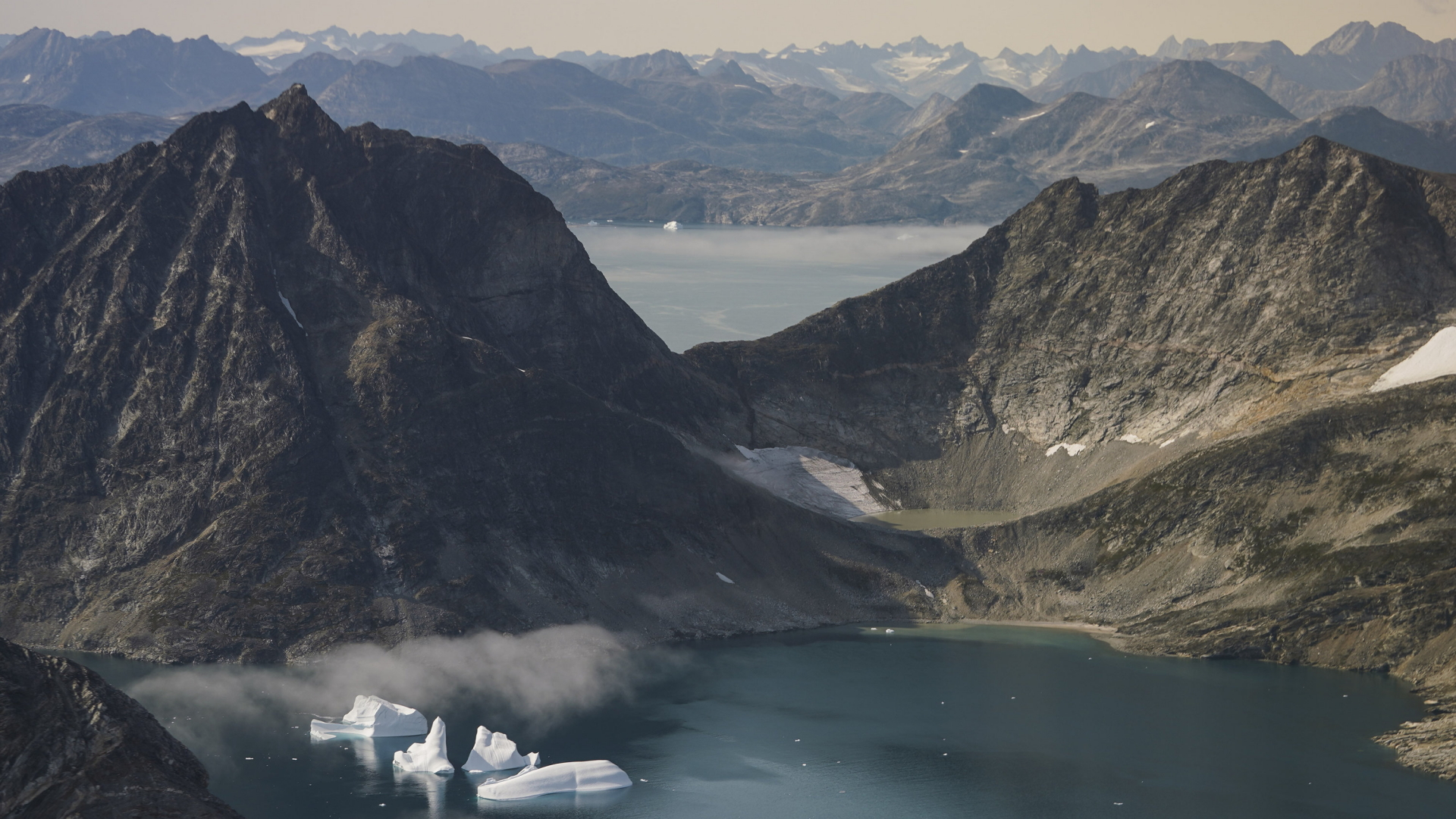  Eisberge treiben zwischen schneefreien Bergen nahe Kulusuk bei Grönland auf dem Wasser. | dpa