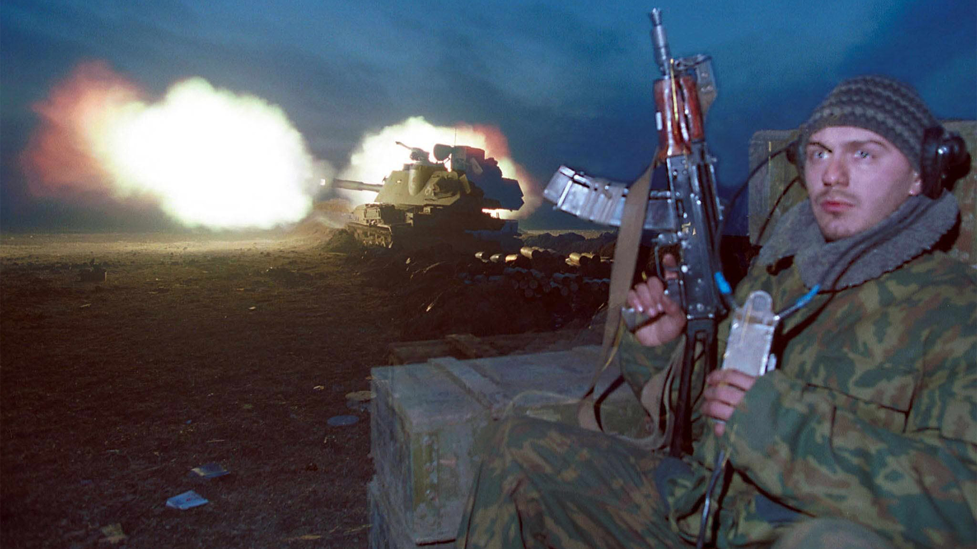 Ein bewaffneter Soldat steht vor einem im Hintergrund brennenden Panzer (Archivbild vom 13.01.2000). | picture-alliance / dpa