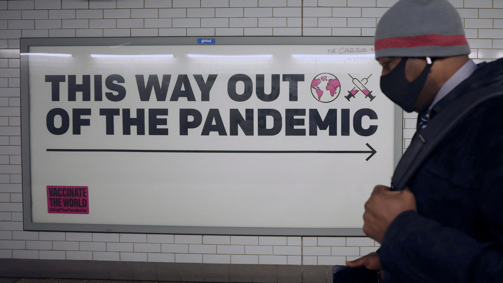 Ein Mann mit Mundschutz geht in London an einem Plakat vorbei mit der Aufschrift: This way out of the pandemic - Das ist der Weg heraus aus der Pandemie