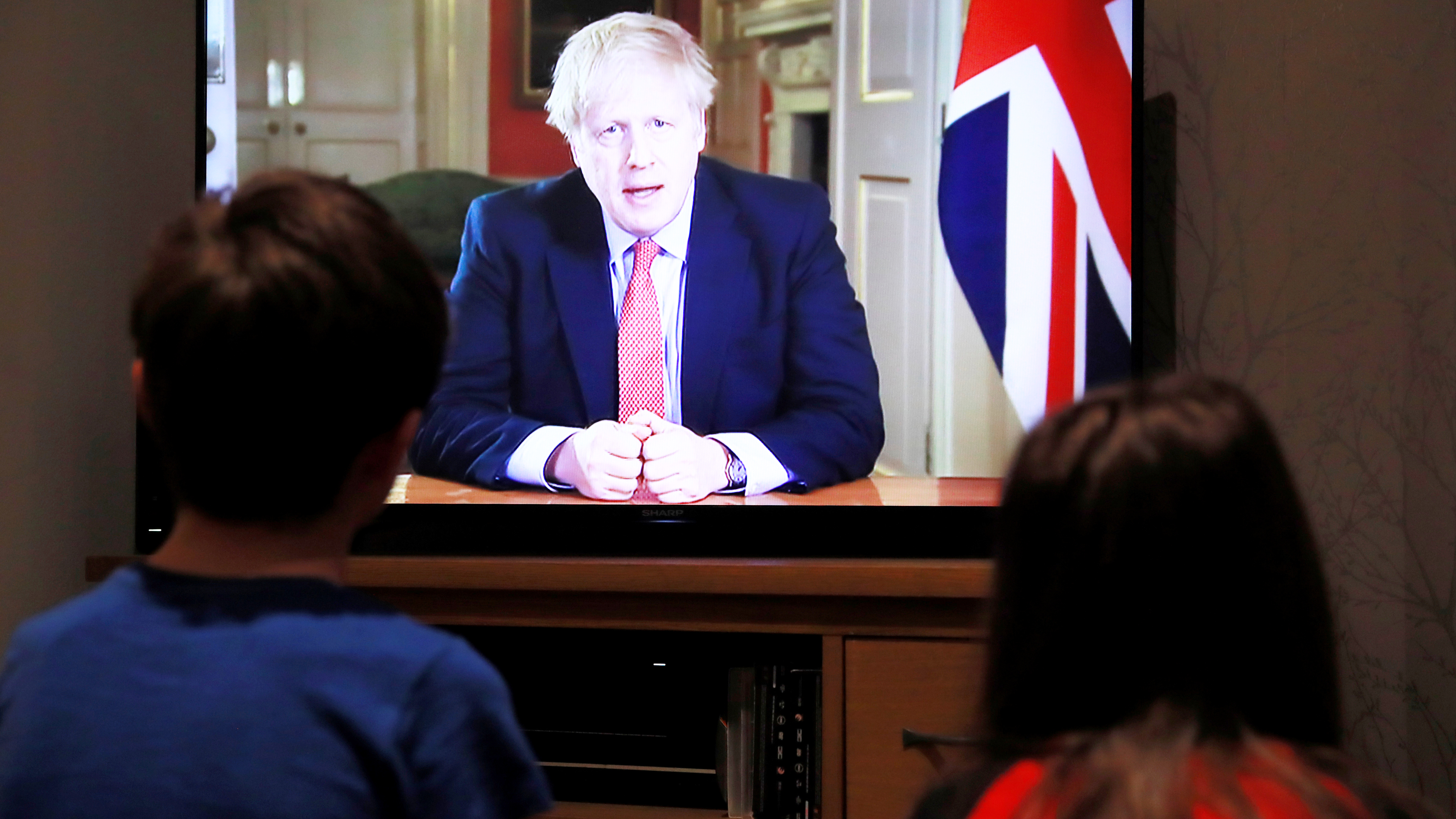 Zwei Kinder sitzen während der Fernsehansprache des britischen Premiers Boris Johnson vor dem Fernseher.