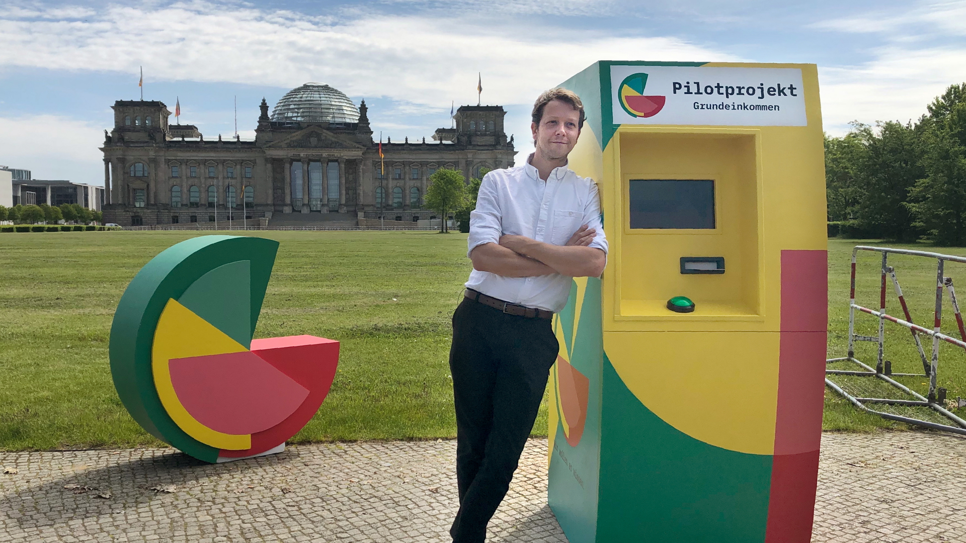 Michael Bohmeyer, Initiator des Vereins "Mein Grundeinkommen", steht an einem symbolischen Geldautomaten, im Hintergrund das Reichstagsgebäude.  | dpa