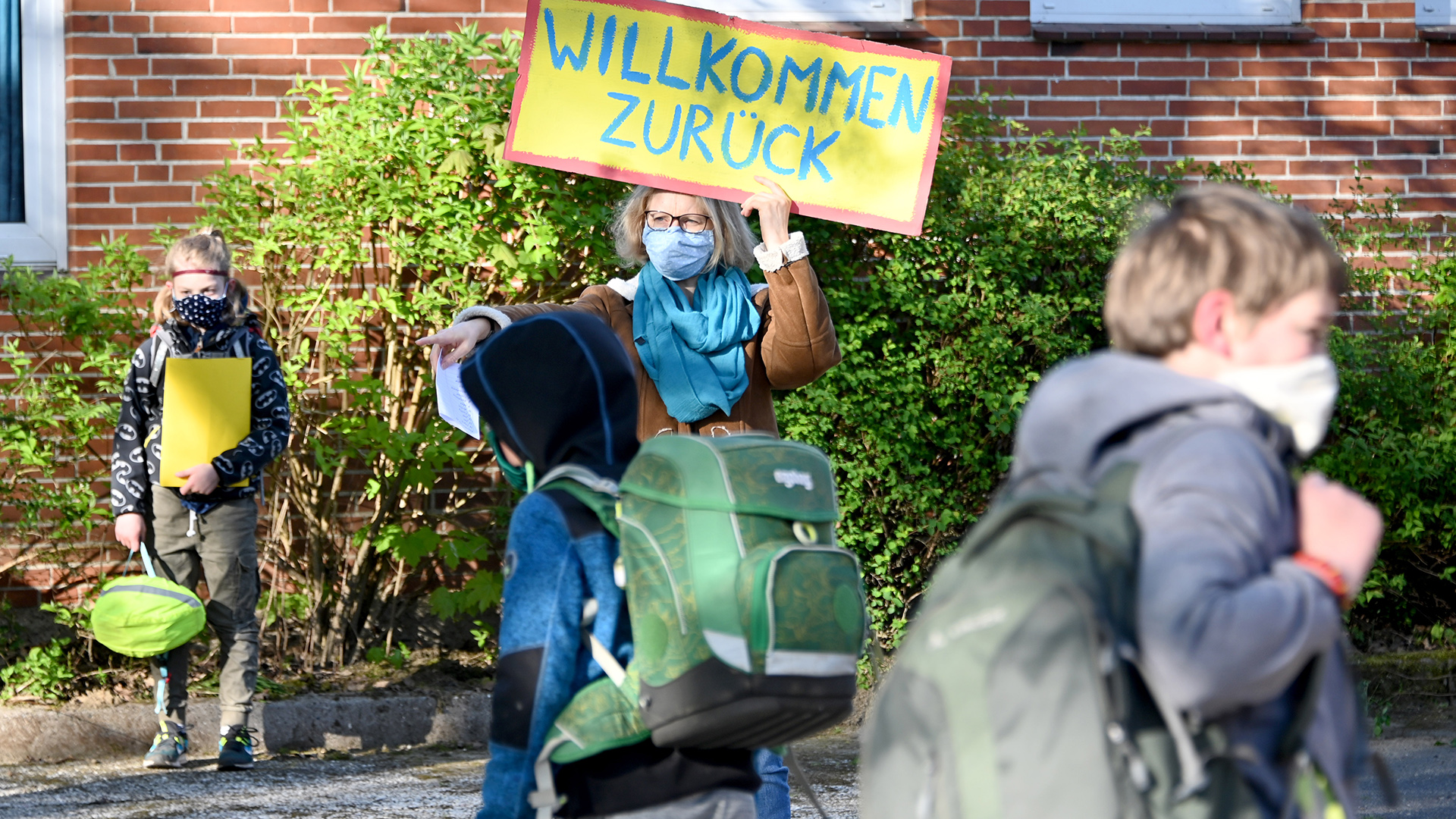 Mit einem Schild ''Willkommen zurück'' begrüßt eine Lehrerin die Viertklässler in der Grundschule in Aukrug. | dpa
