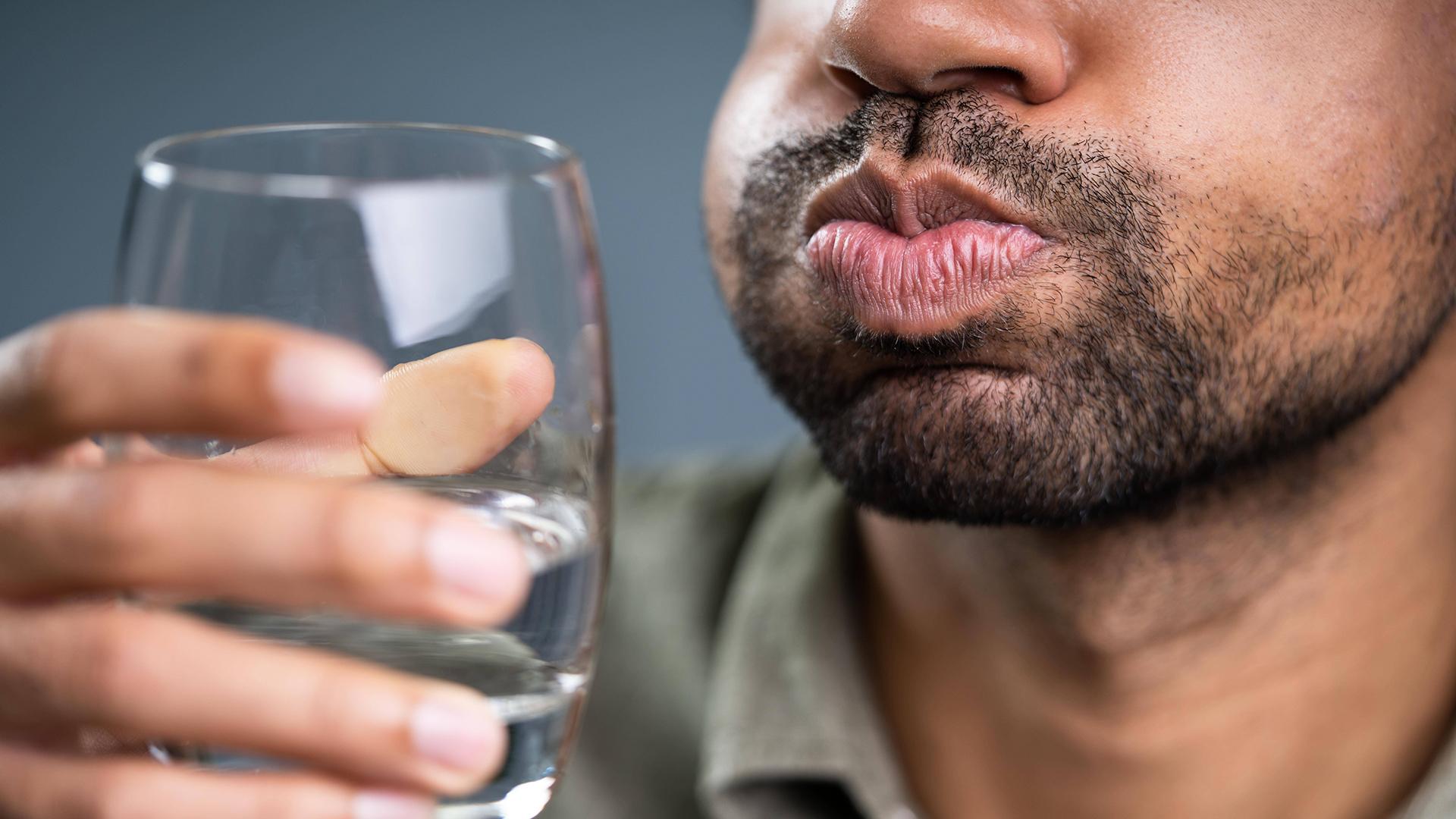 Ein Mann hält ein Glas mit Flüssigkeit in der Hand und gurgelt | imago images/Panthermedia