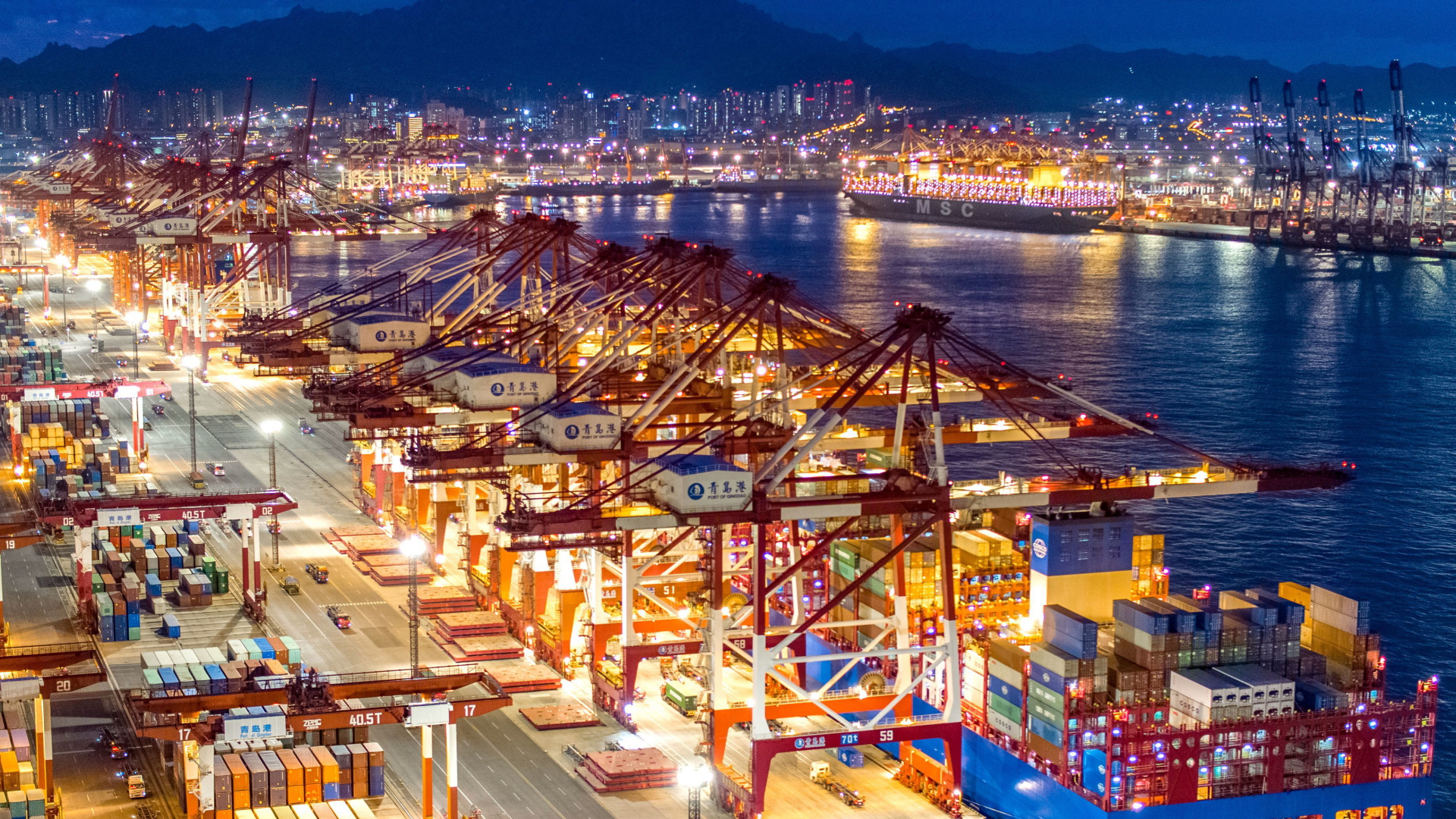Containerschiffe liegen im nächtlich beleuchteten Containerterminal des Hafens von Qingdao. | dpa
