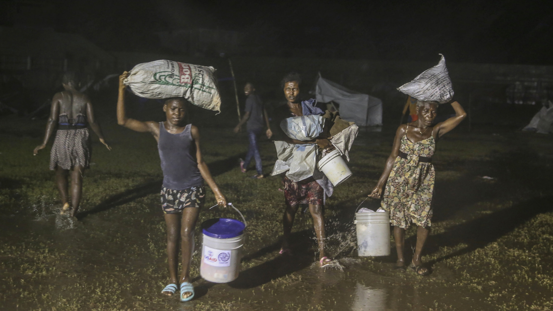 Menschen gehen bepackt mit ihrem Hab und Gut unter dem Regen des Tropensturms "Grace" in ein Flüchtlingslager in Les Cayes. | AP