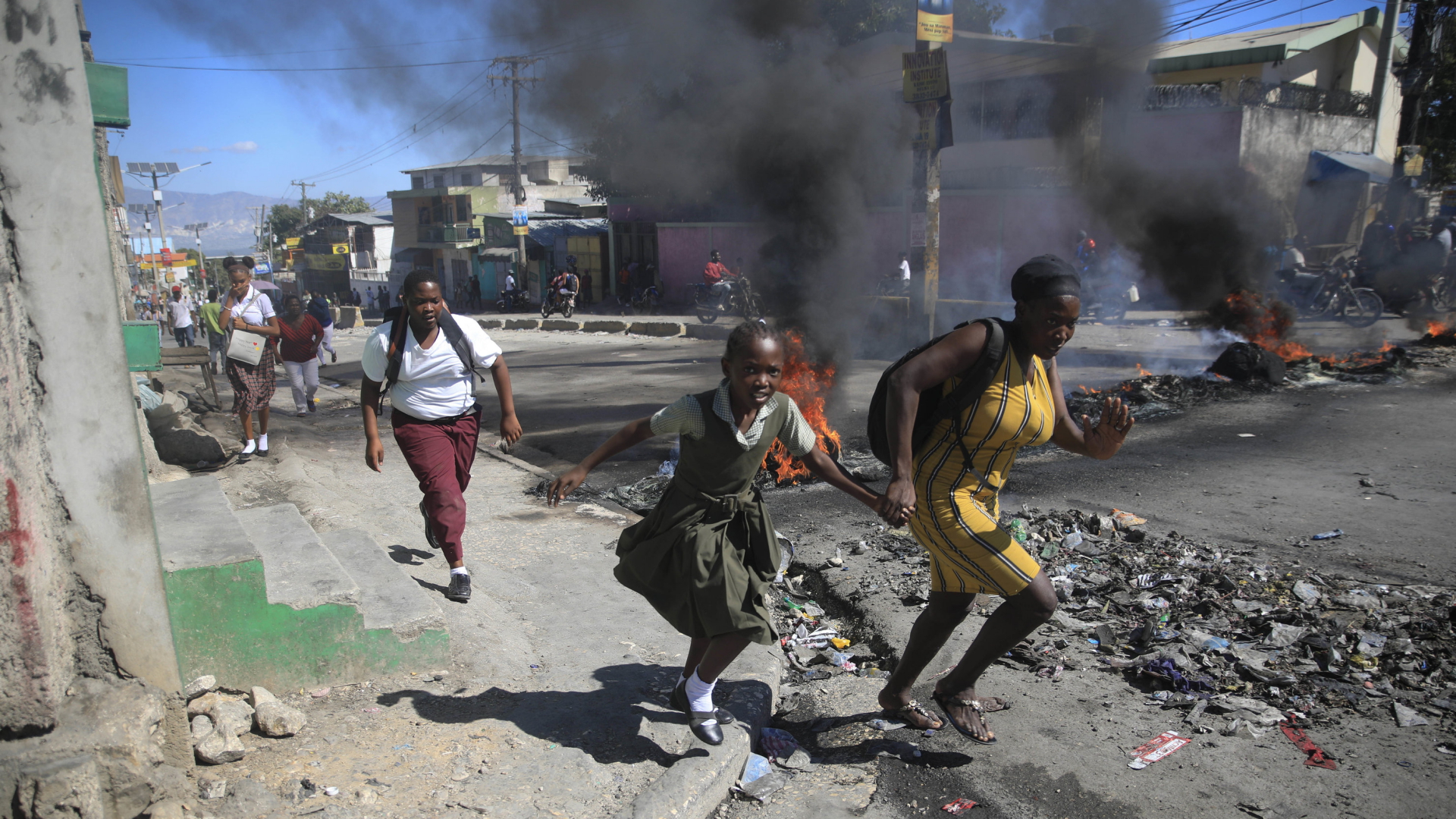 Eine Frau und eine Tochter rennen entlang einer brennende Barrikade in Port-au-Prince (Haiti) | AP