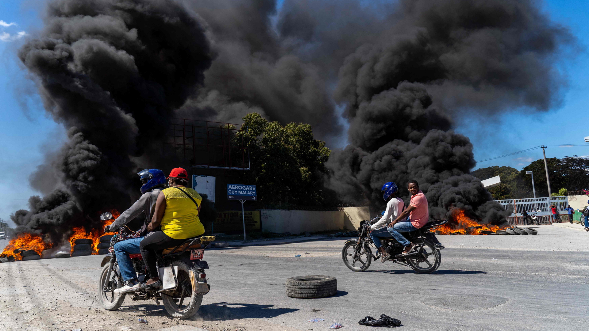 Motorradfahrer fahren in Port-au-Prince (Haiti) an Barrikaden aus brennenden Autoreifen vorbei. | AFP