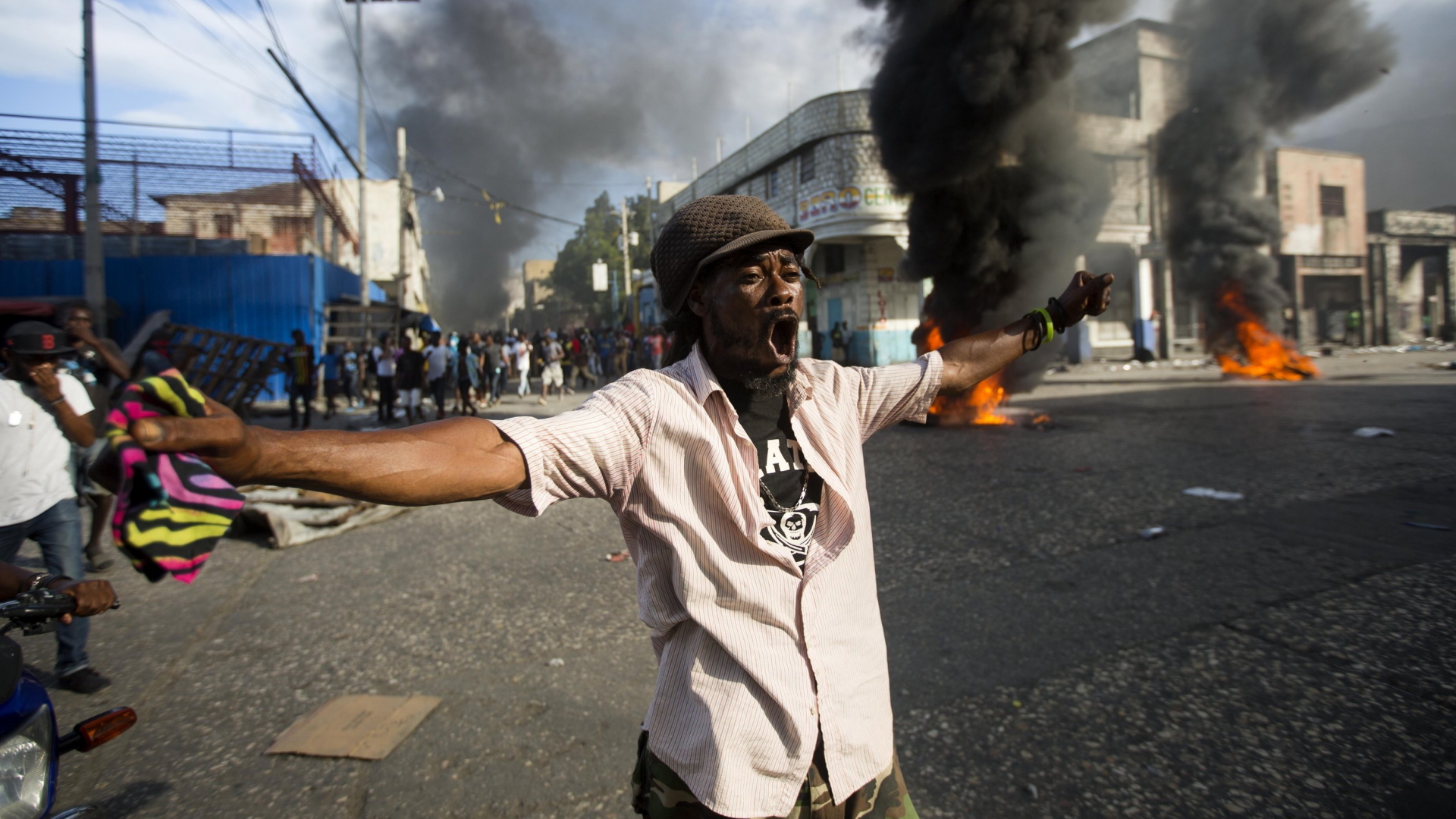 Ein Demonstrant ruft Parolen gegen die haitianische Regierung. Im Hintergrund stehen brennende Barrikaden. | Bildquelle: AP