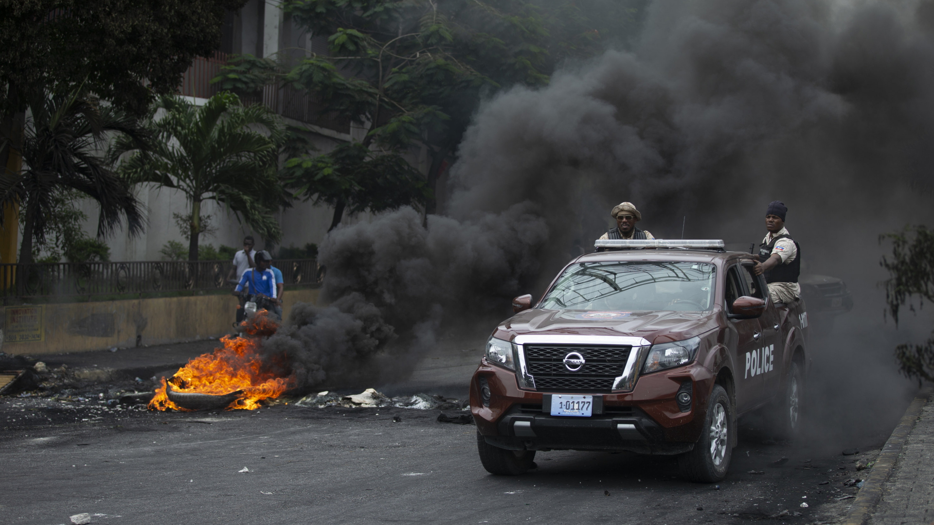 Ein Fahrzeug mit der Aufschrift "Police" passiert Port-au-Prince eine brennende Straßensperre.  | AP