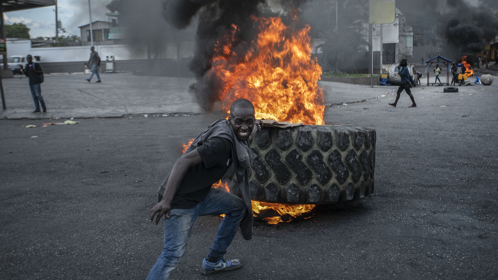 In Haiti steht ein Mann vor einem brennenden Autoreifen. | AP