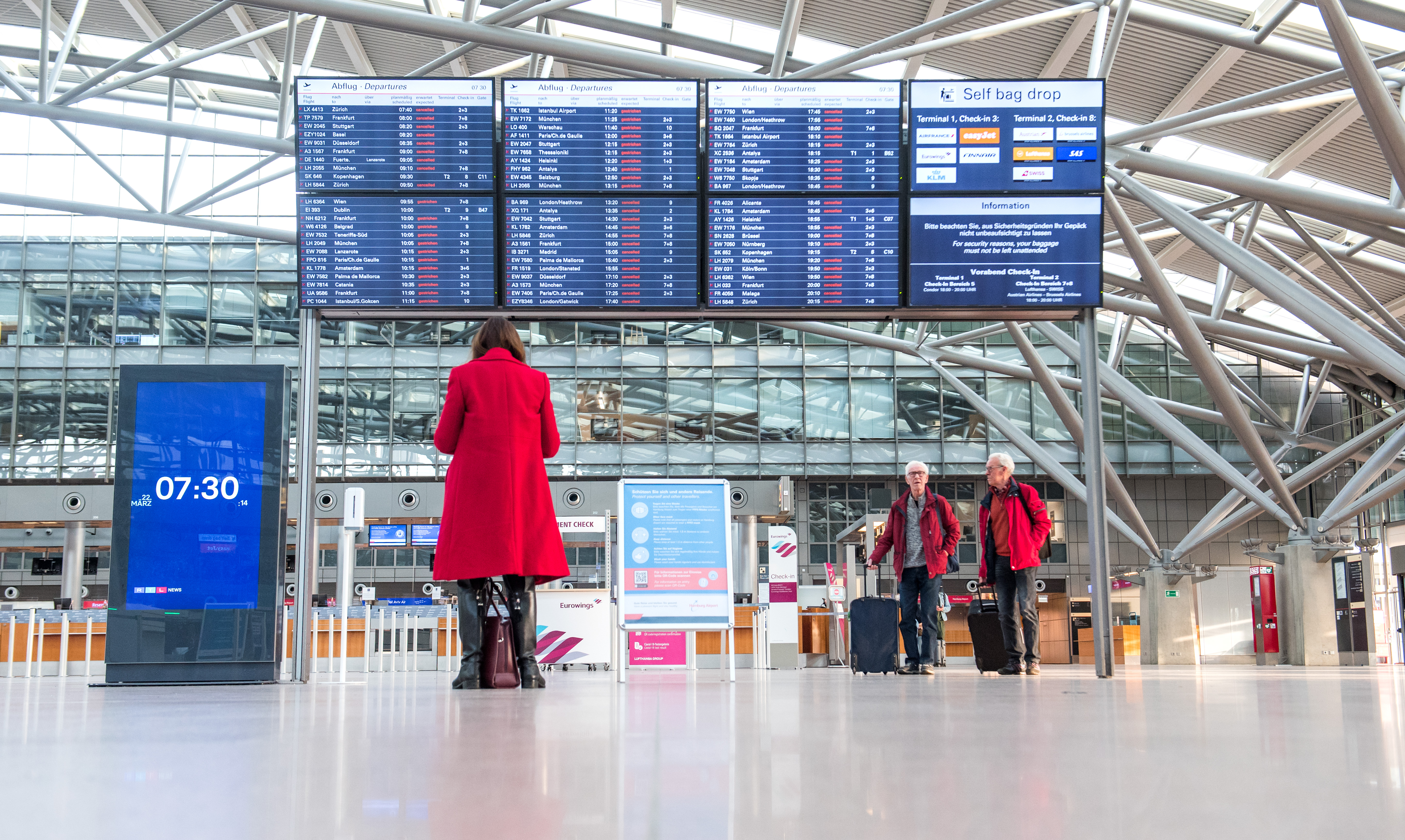 Reisende stehen am Flughafen Hamburg vor einer Anzeigetafel. | dpa