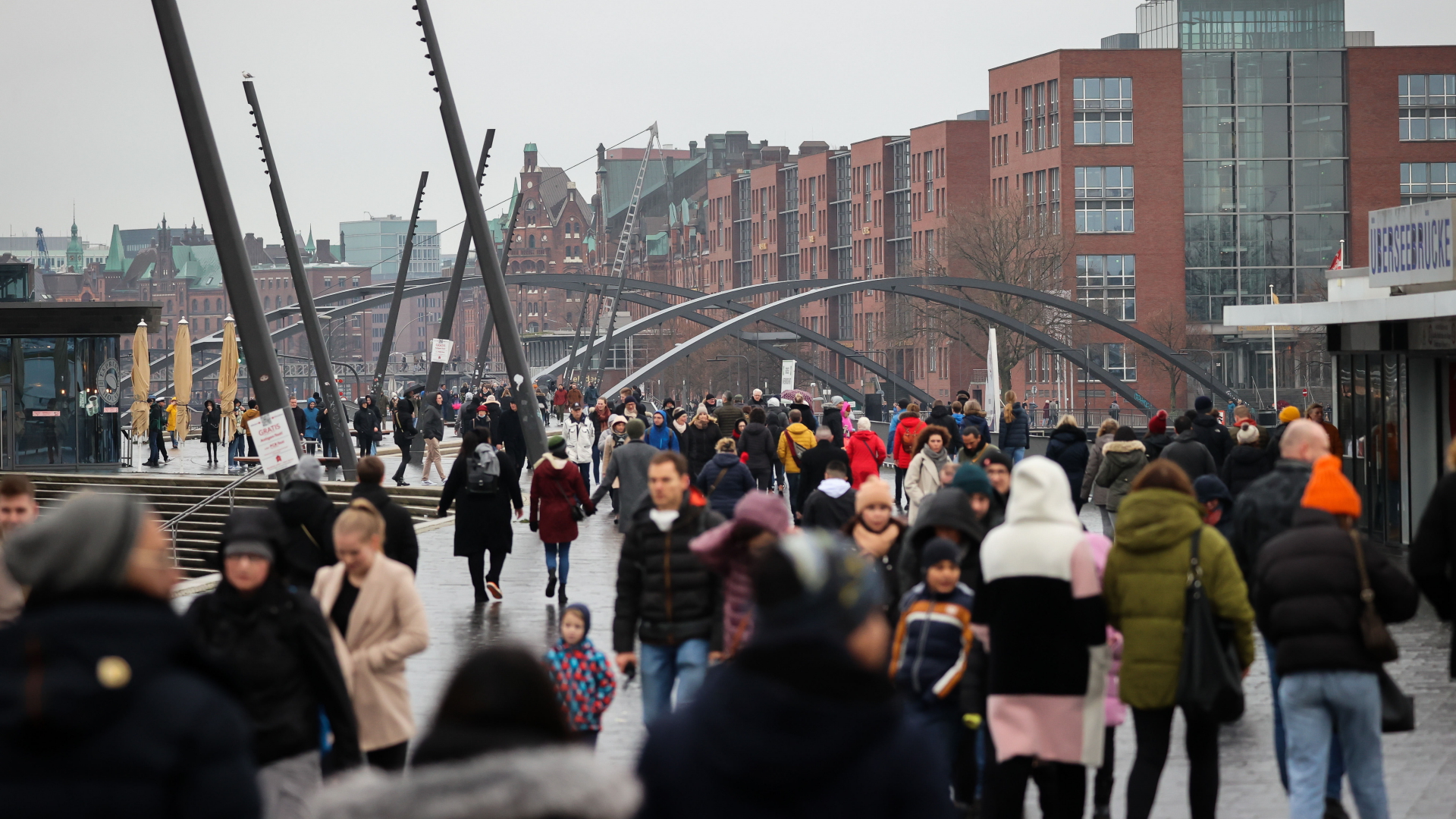 Passanten gehen in Hamburg bei leichtem Regen auf der Elbpromenade an den Landungsbrücken spazieren.