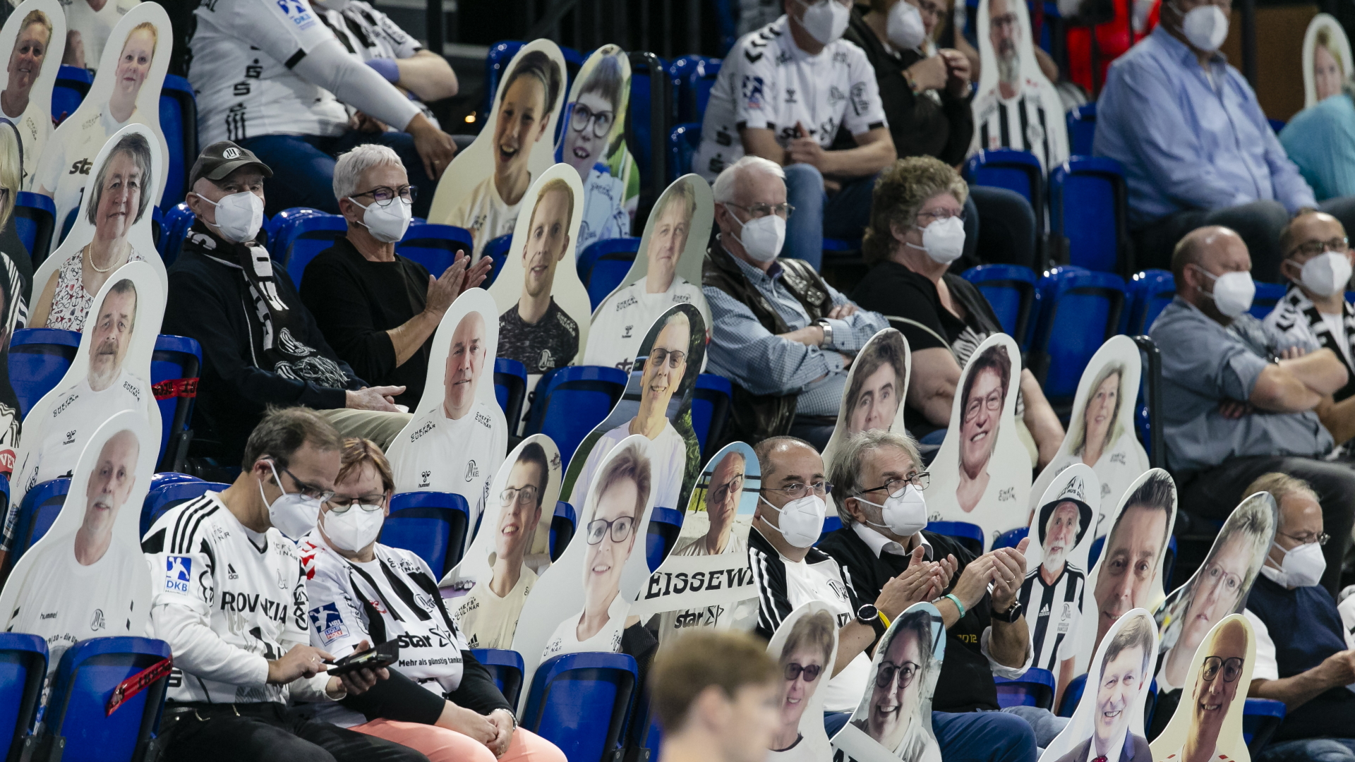 Zuschauer sitzen bei einem Handballspiel zwischen Pappfiguren, auf denen Gesichter von Fans zu sehen sind. | dpa