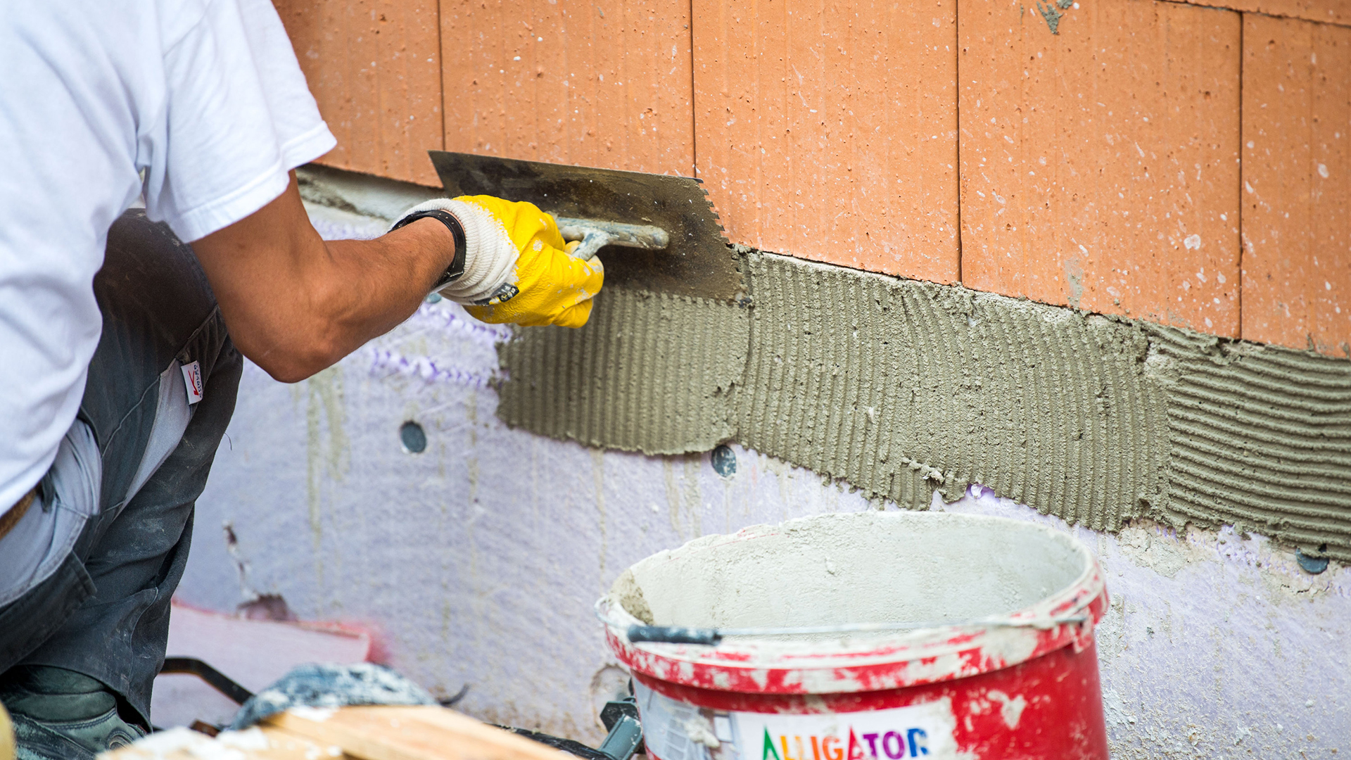 Ein Maurer trägt auf einer Baustelle Klebemörtel auf eine Wand auf. | dpa