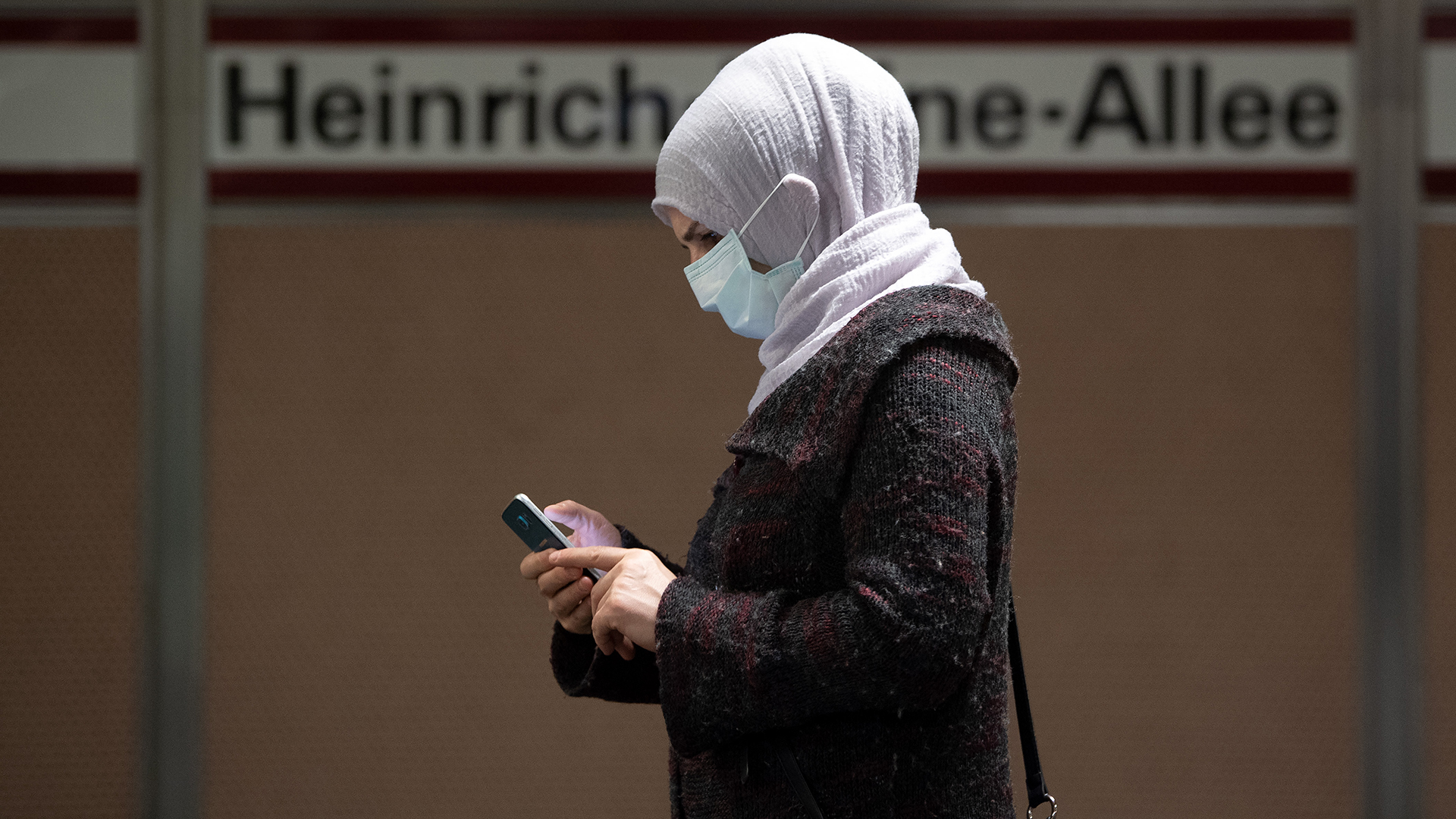 Eine Frau steht mit Mundschutz am Bahnsteig und bedient ihr Smartphone | dpa