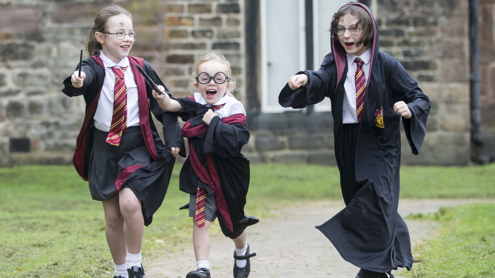 Drei Kinder in Harry-Potter-Kostüm stürmen begeistert über einen Weg. | dpa