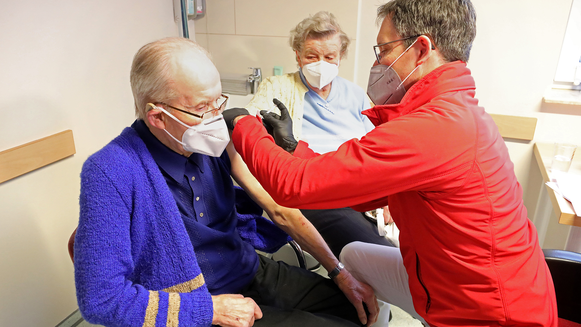 In einer Hausärztlichen Gemeinschaftspraxis erhalten zwei ältere Patienten die erste Corona-Schutzimpfung.