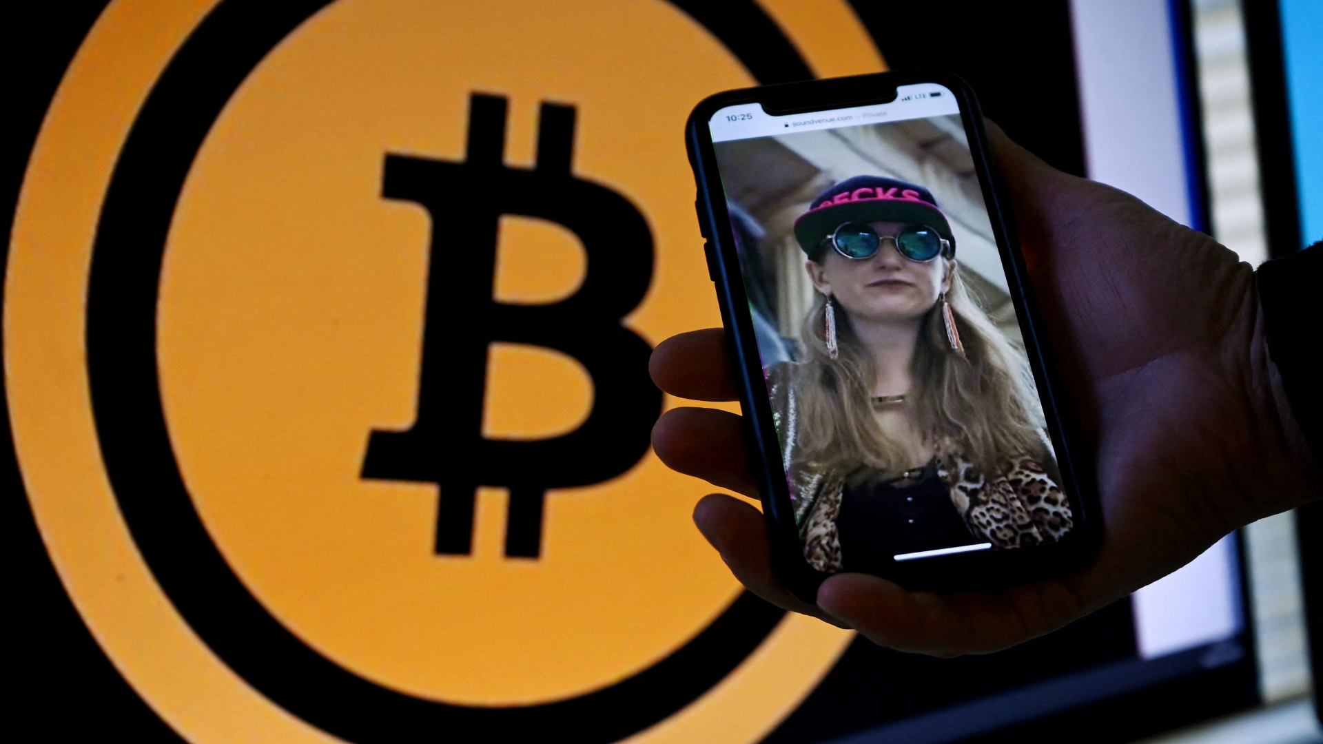 Heather Morgan ist auf einem Smartphone vor einem Bitcoin-Symbol zu sehen