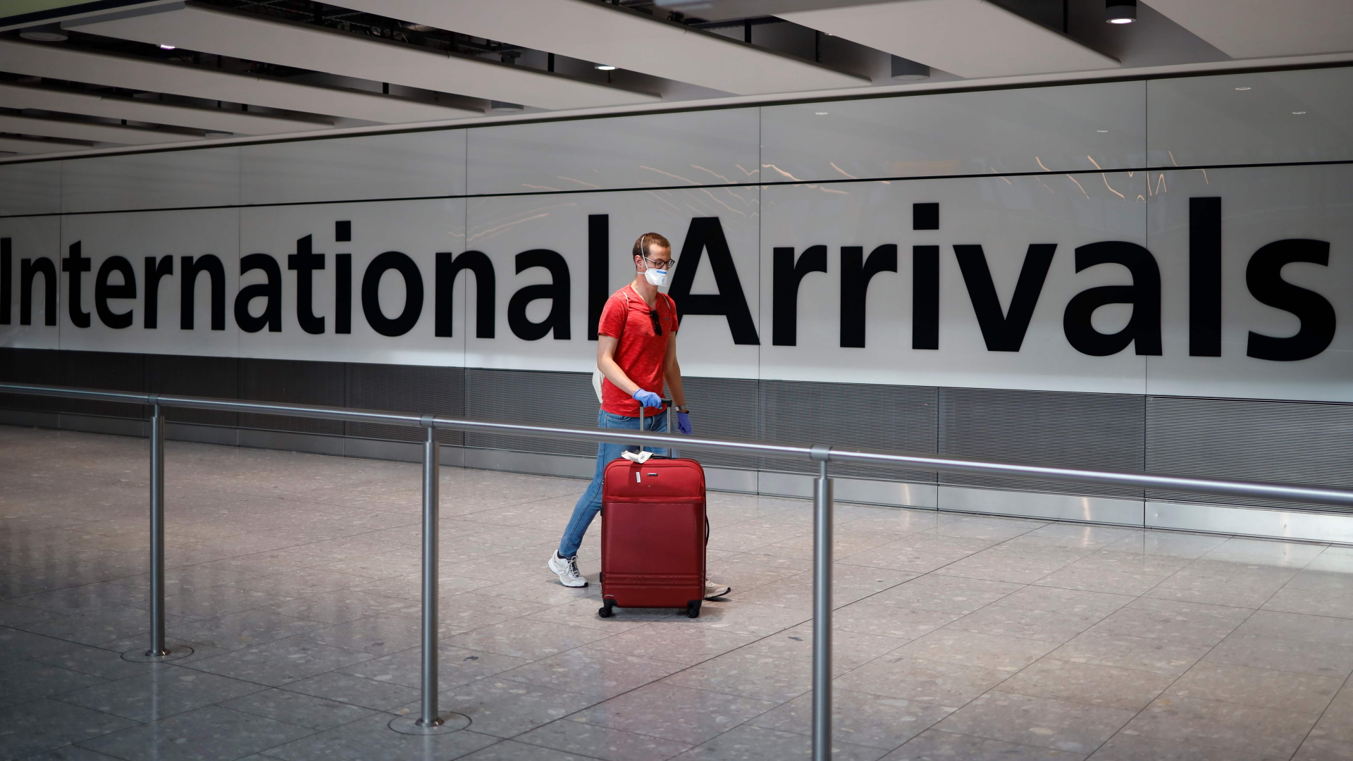 Ein Mann mit Gesichtsmaske zieht am Flughafen Heathrow in London einen Koffer hinter sich her. | AFP