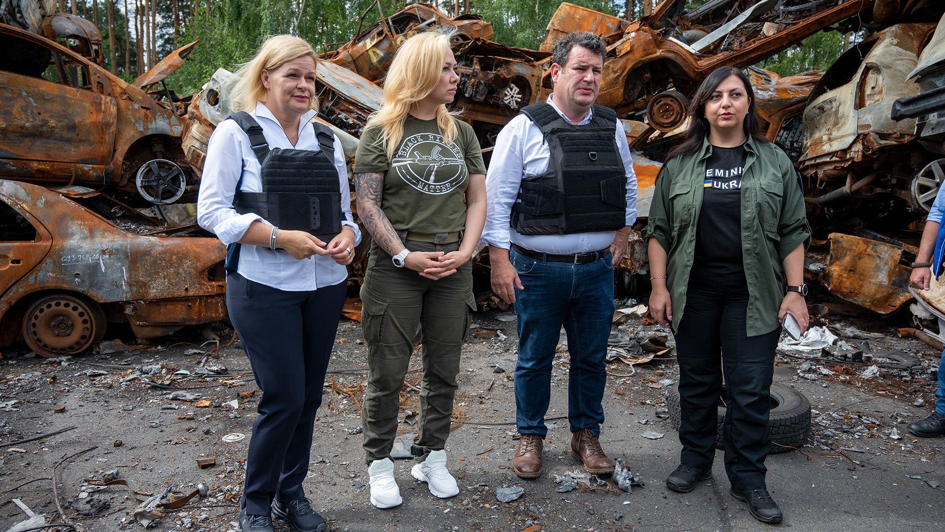 Nancy Faeser, Hubertus Heil, Mary Akopjan (r) und Anzhela Makeiewa (2.v.l), stehen vor zerstörten Autos in Irpin (Ukraine). | dpa