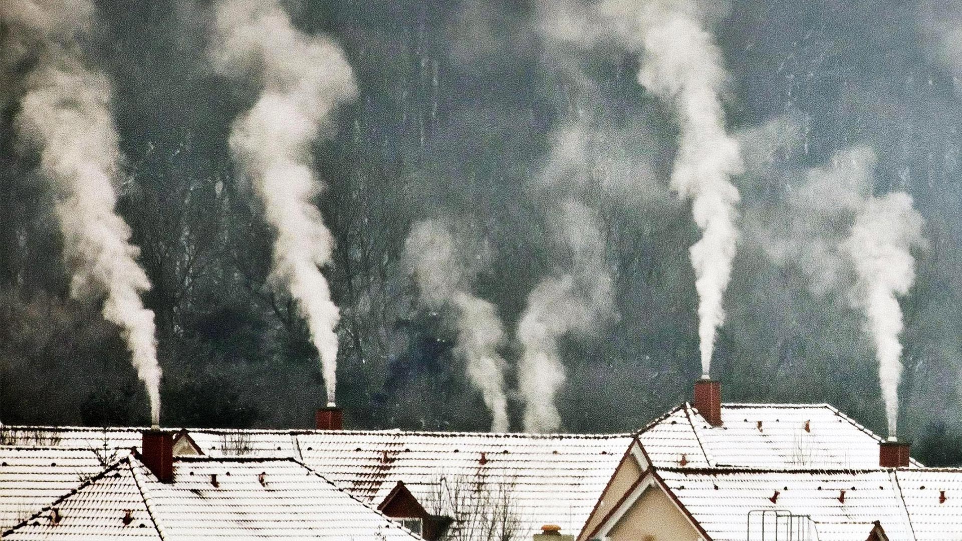 Qualm steigt in kalter Luft aus Schornsteinen auf Hausdächern.