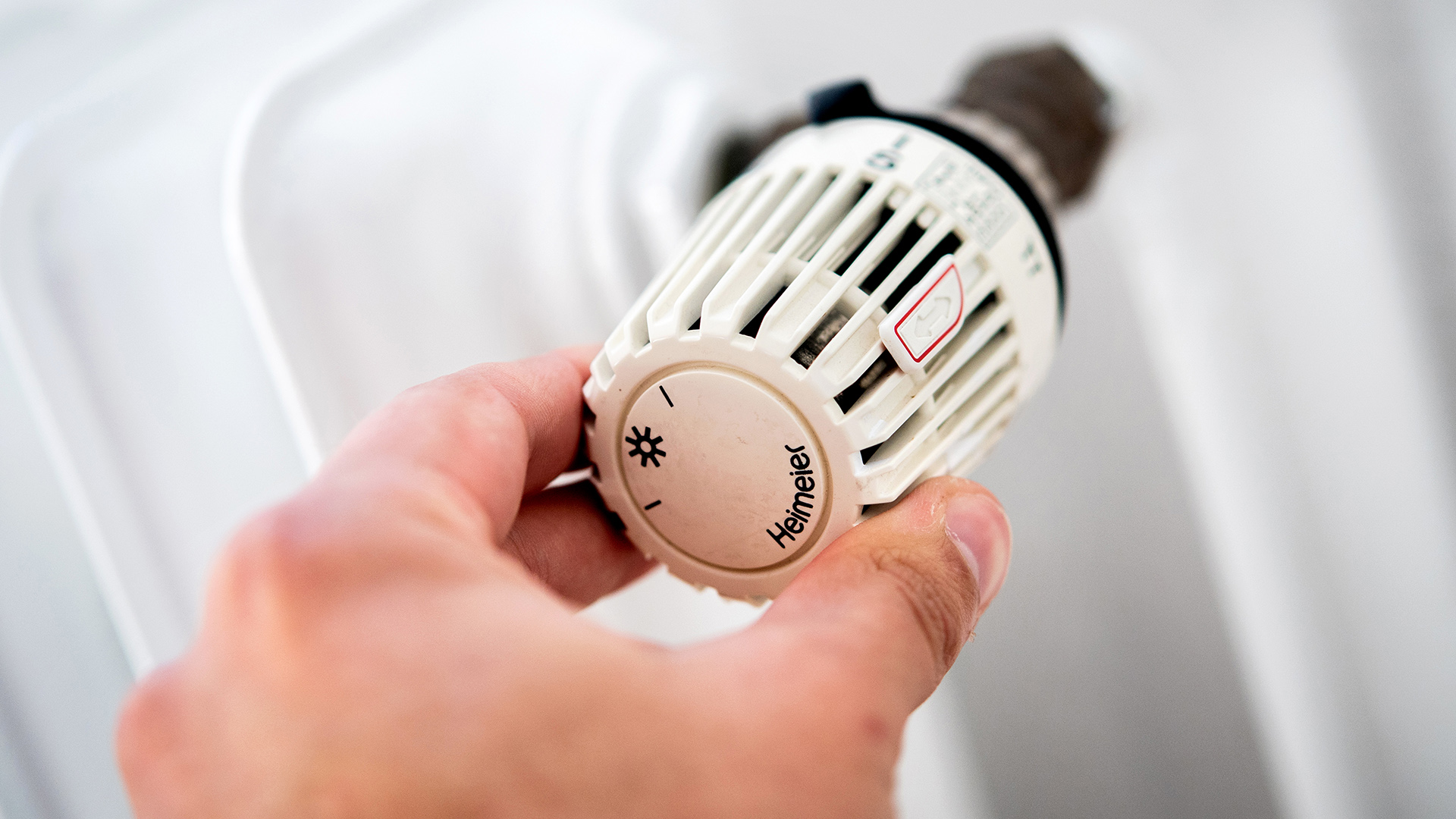 Ein Mann dreht in einer Wohnung am Thermostat einer Heizung. | dpa