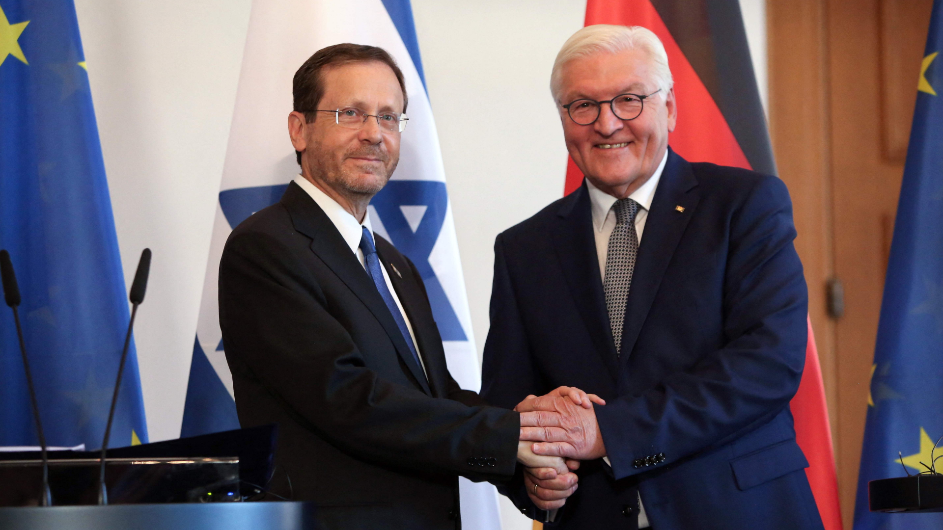 Isaac Herzog und Frank-Walter Steinmeier schütten sich vor einer deutschen und einer israelischen Fahne die Hände. | AFP