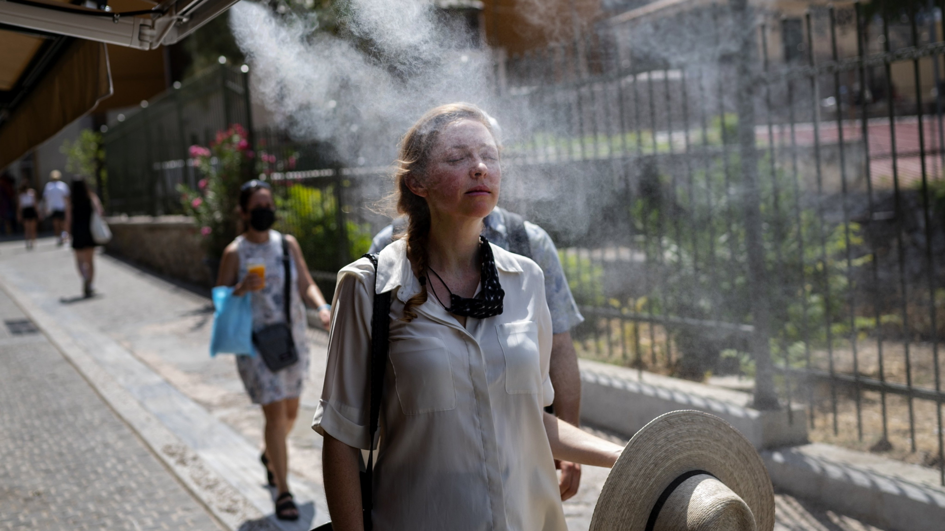 Eine Frau geht durch einen Sprühnebel, um sich in der großen Hitze zu erfrischen. | dpa
