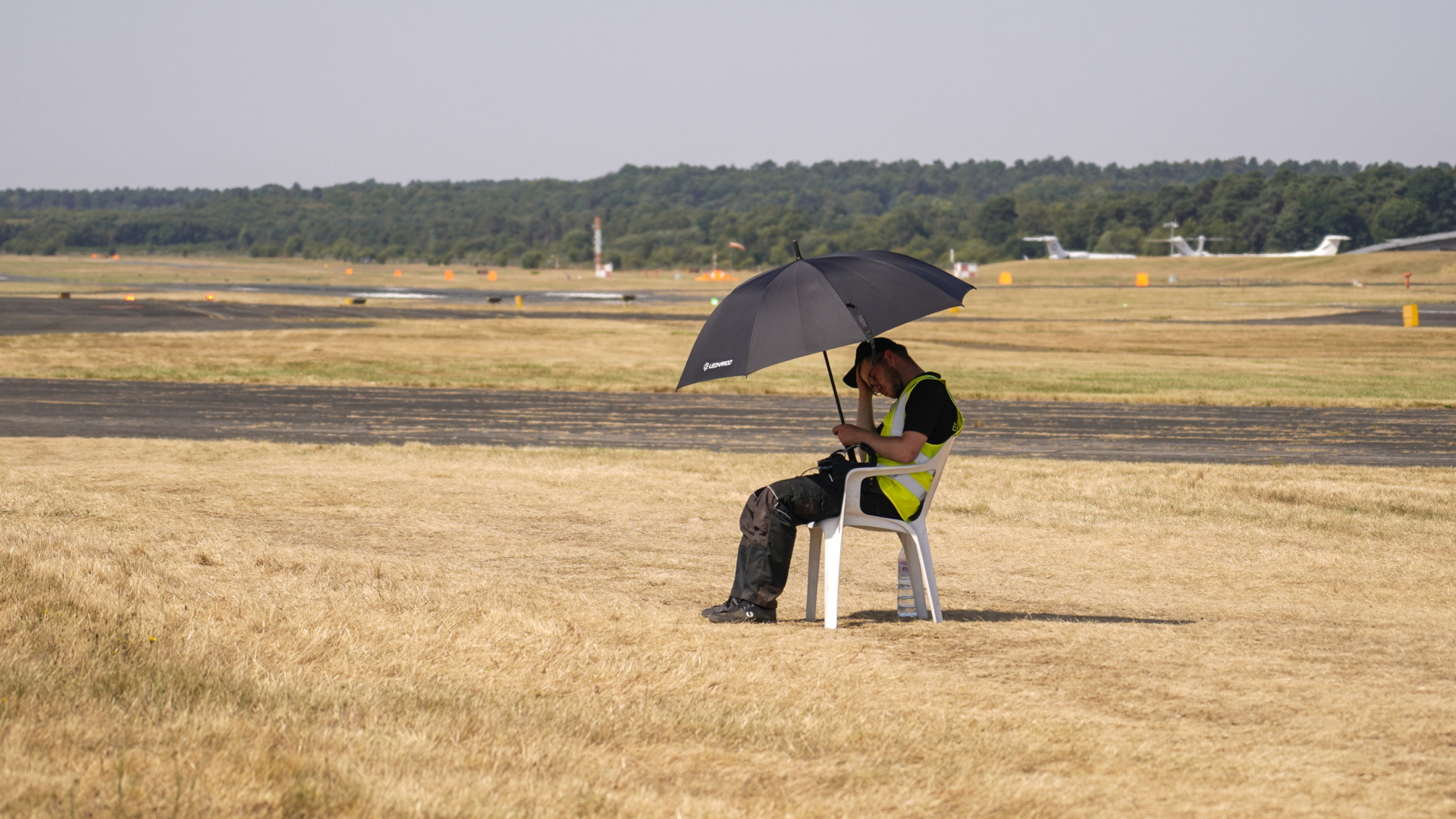 Ein Arbeiter in Farnborough, England, sucht auf freiem Geländer Schutz vor Hitze und Sonne unter einem Schirm. | AP
