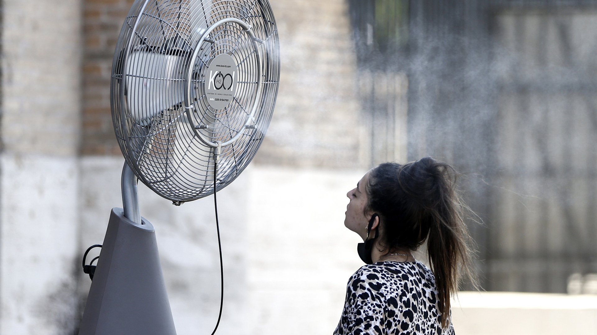 Eine Frau erfrischt sich an einem Ventilator mit Wassernebel neben dem Kolosseum in Rom. | dpa
