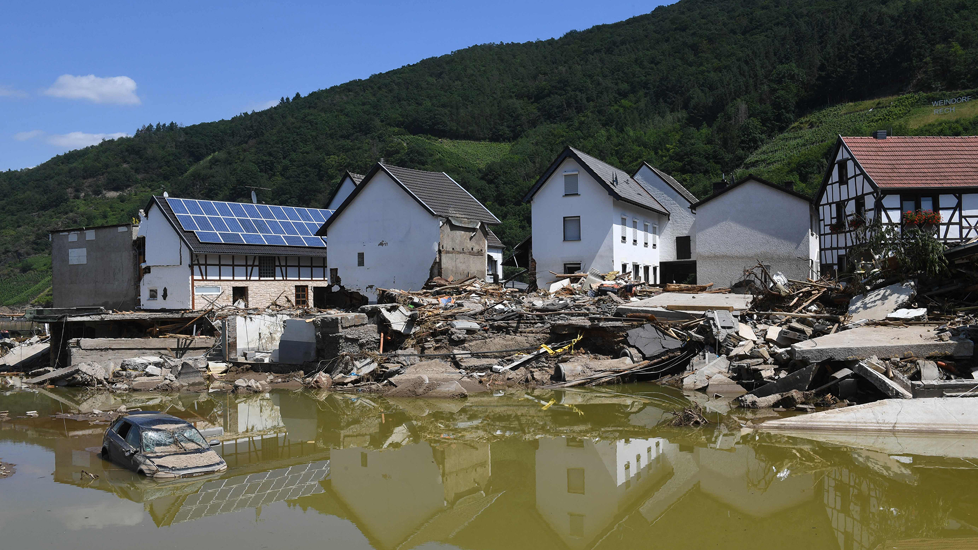 Zerstörte Häuser werden im braunen Hochwasser reflektiert. | AFP