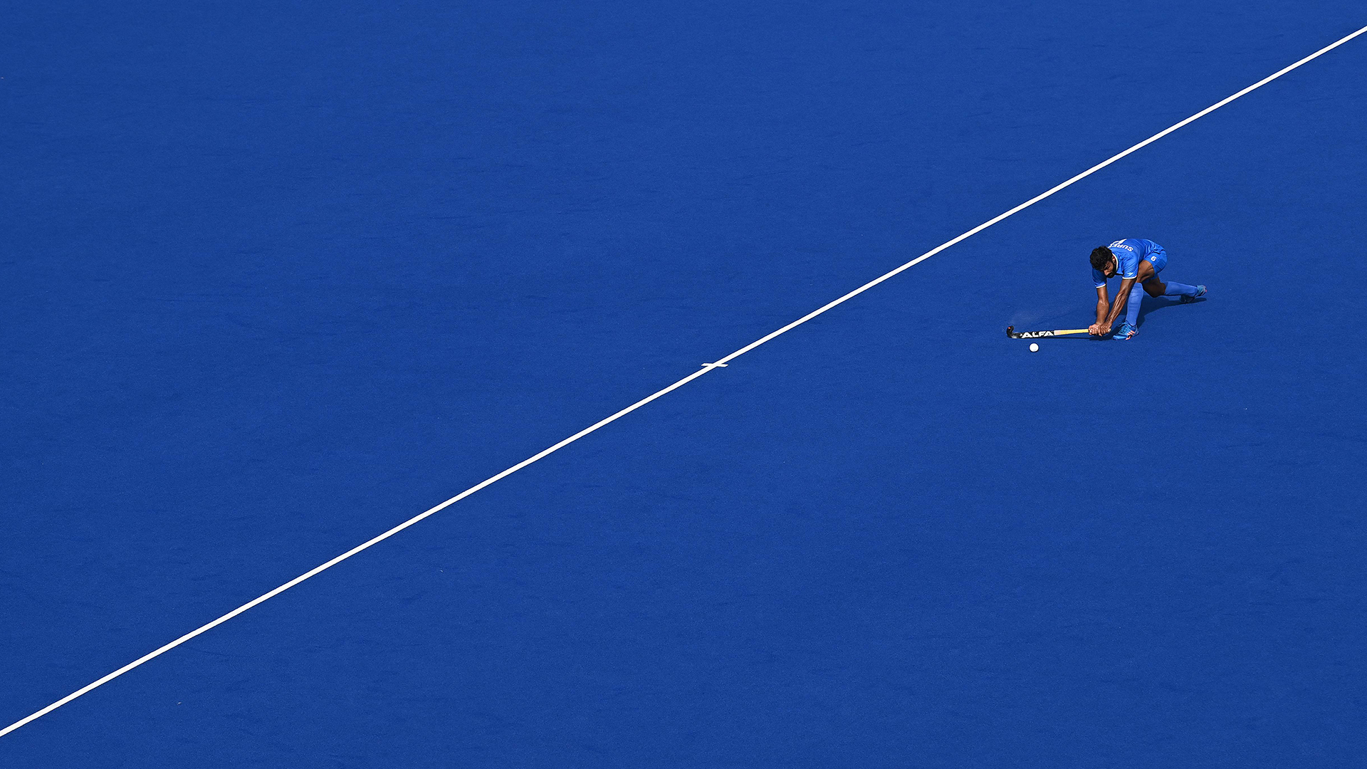 Ein Hockeyspieler schlägt einen Pass auf blauem Grund neben einer weißen Linie. | AFP