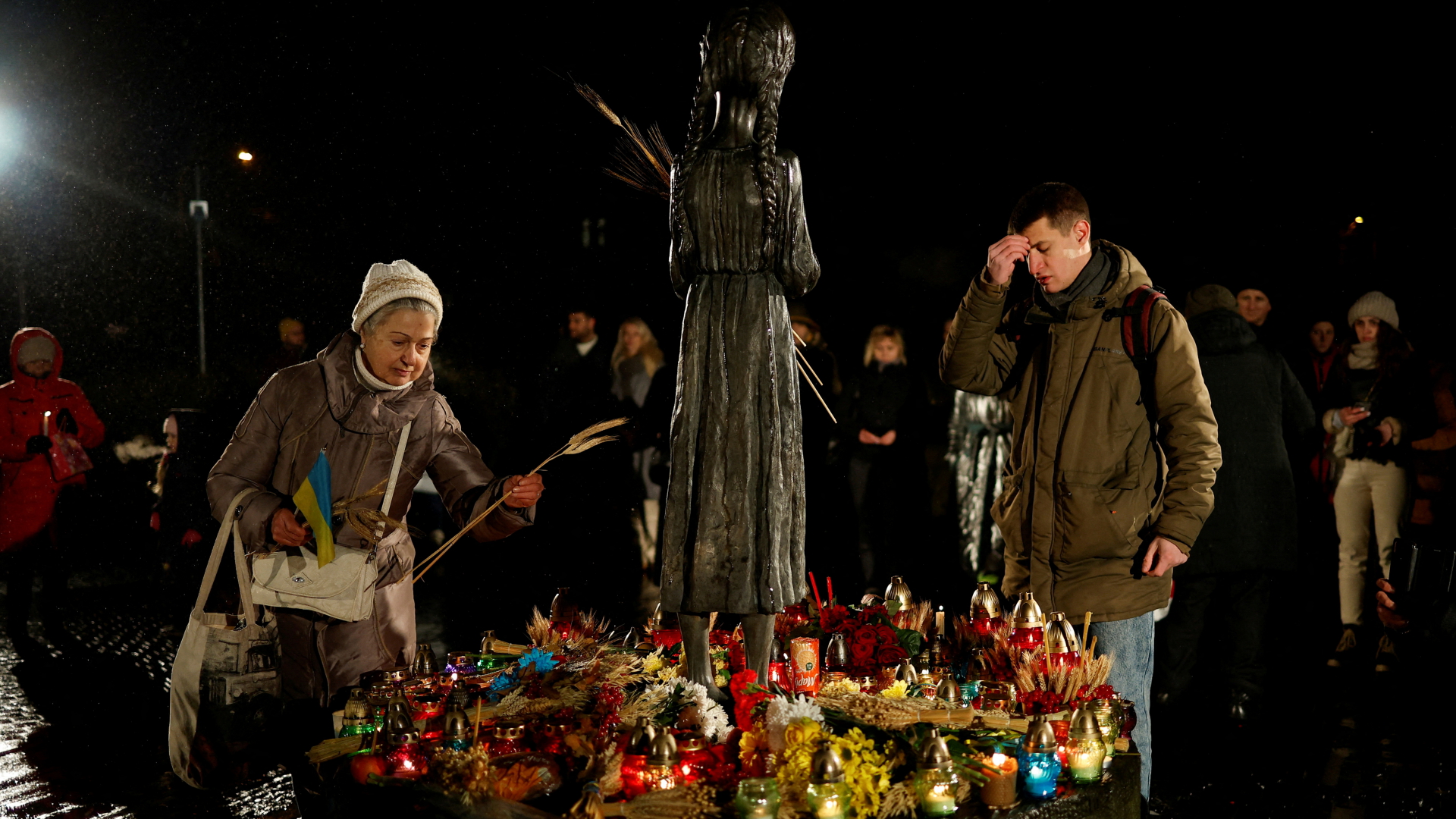 An einer Statue in Kiew legt eine Frau während einer Zeremonie zum Gedenken an die große Hungersnot eine Weizenähre nieder, ein Mann betet.  | REUTERS